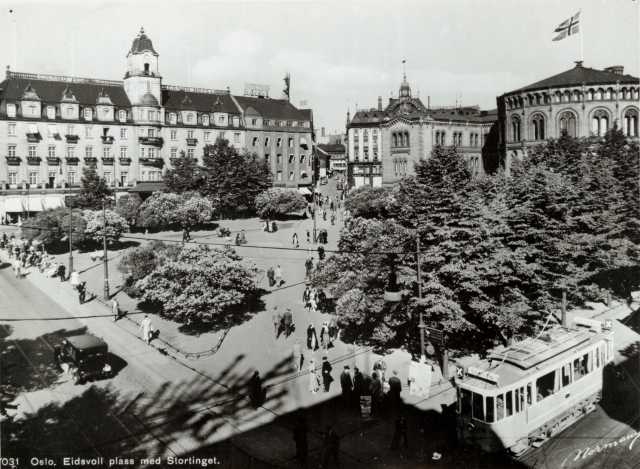 Avfotografert postkort. Eidsvoll plass i Oslo med mennesker, Stortinget til høyre, Grand Hotell i bakgrunnen og i Stortingsgata kjører en trikk.