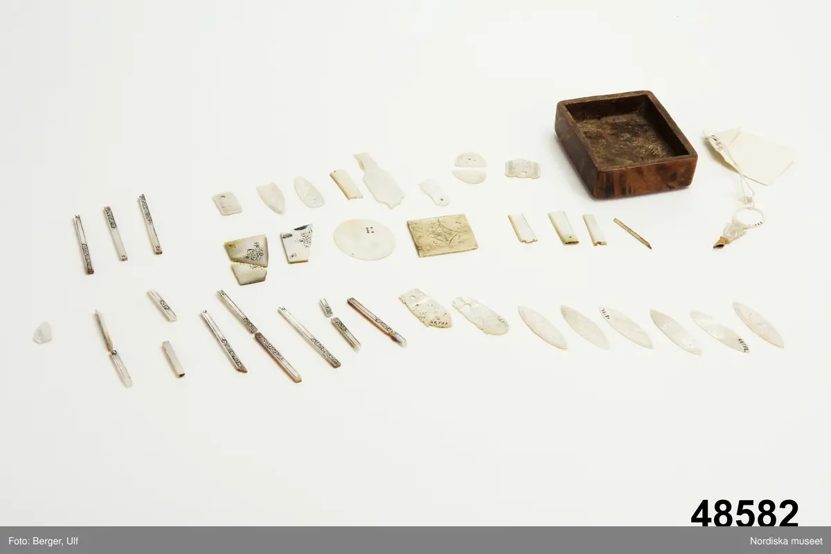 Brädspelslåda för bräde, kvarn och schack, med sju spelbrickor. Svart fanér med inläggningar av pärlemor, elfenben samt graverade förgyllda metallskivor. Blindträ av ek. (Uppgifter från katalogkort). Tillhörande träask för förvaring av spelpjäserna.