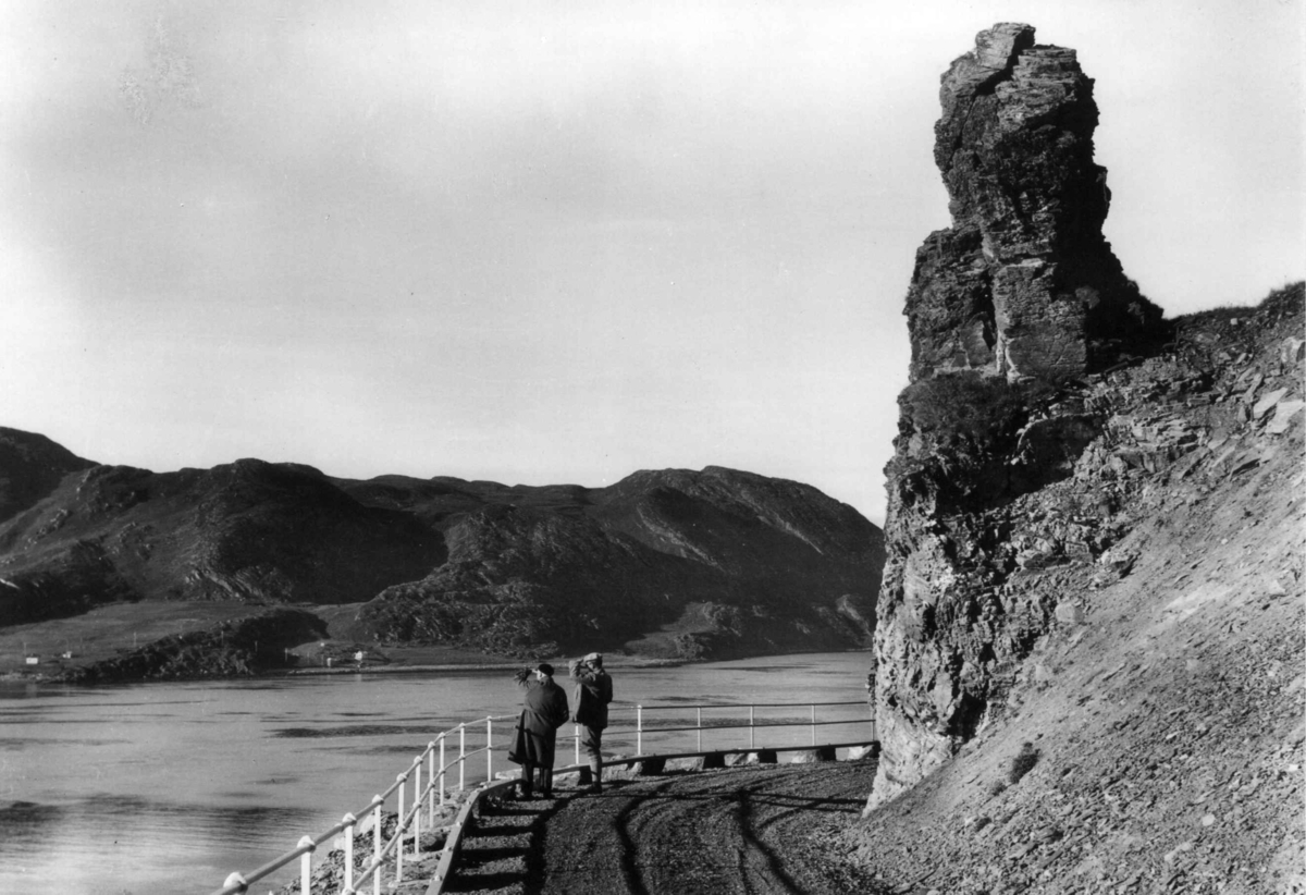 Stallo el. Áhkanjárstábba, gammel samisk offerstein, nedenfor en vei med to personer. Fálesnuorri / Kvalsund, Finnmark.