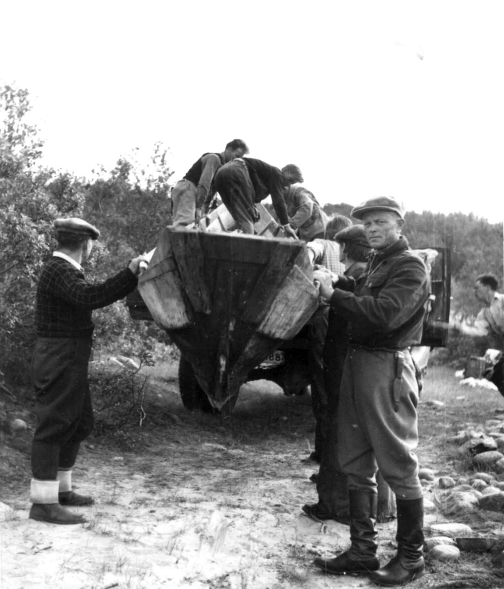 Båt og bagasje kjøres med lastebil forbi Storfossen i Tana, mange personer hjelper til. 1952.