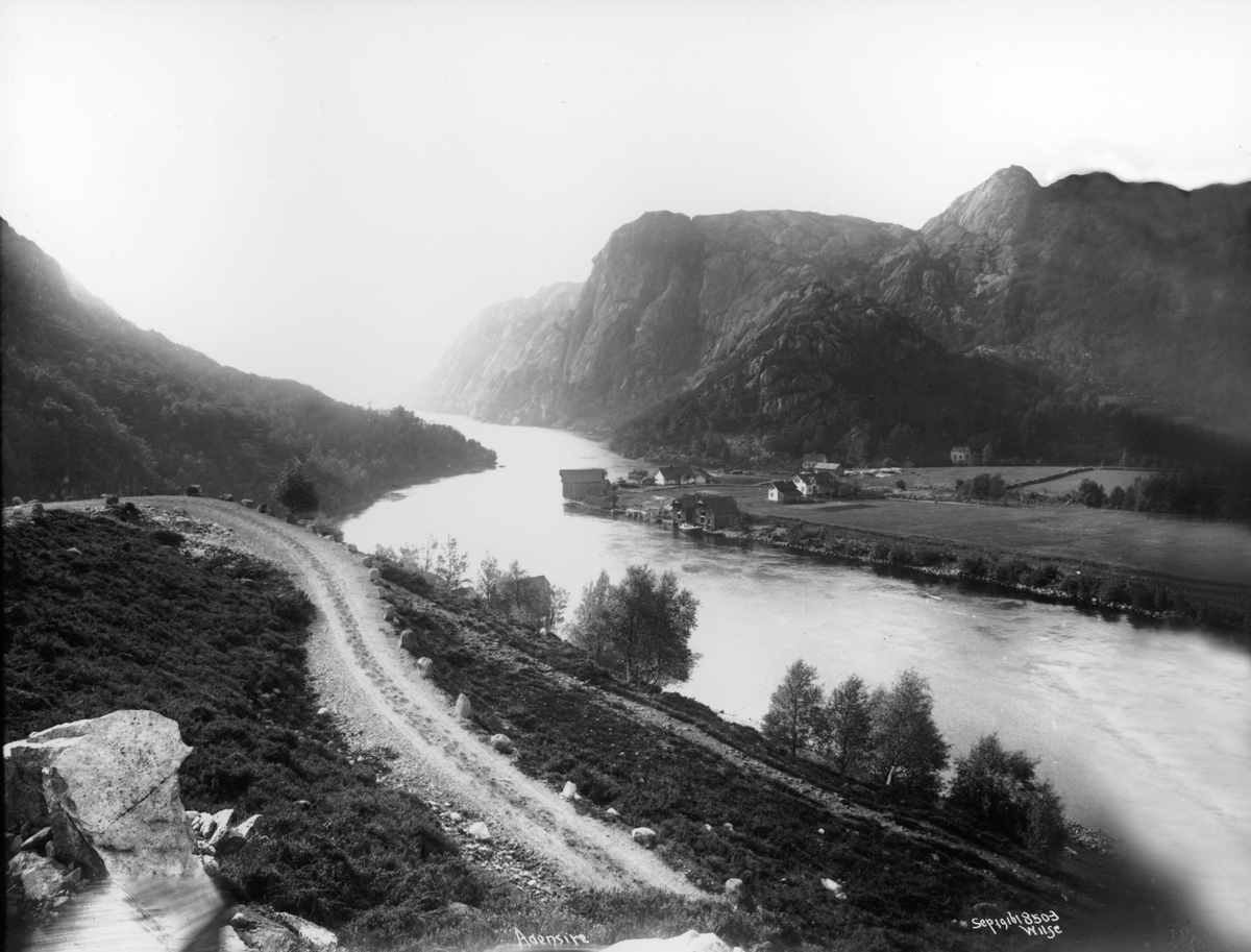 Landskap, med fjell- og fjordparti og bebyggelse, Åna-Sira, Sokndal, Rogaland. Flere gårdsbruk, bryggepartier med sjøboder. Veiparti i forgrunnen.