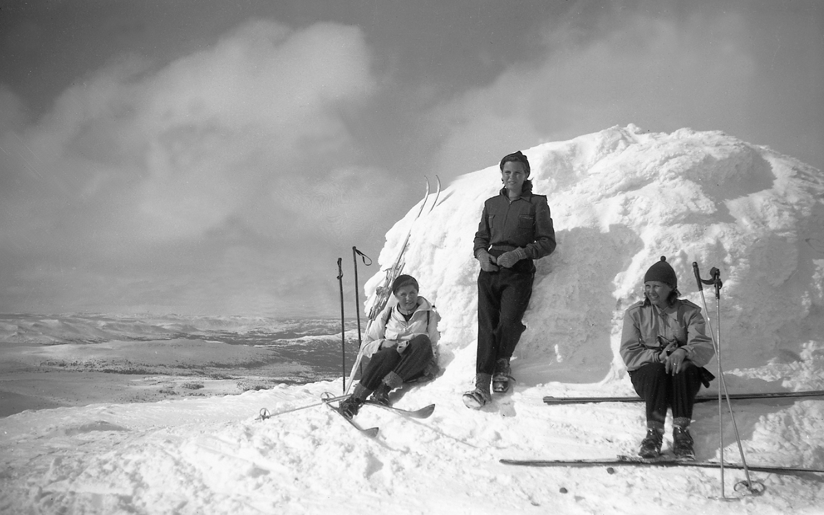 Tre skikledde damer sitter lent mot Gråfjell, Norefjell. Fotografert 1947.