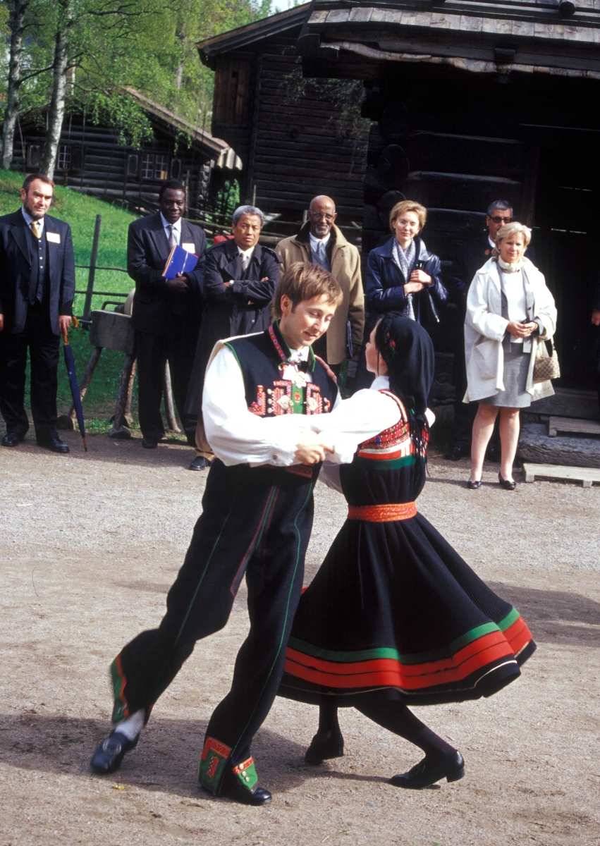 Norsk Folkemuseums dansegruppe, kledd i setesdalsdrakter, danser folkedans i Numedalstunet på Norsk Folkemuseum. Et par danser  i forgrunnen mens publikum ser på.