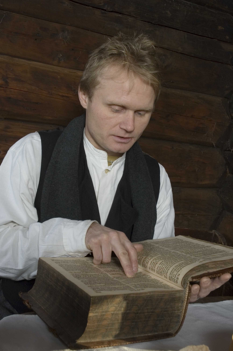 Høytlesning fra Bibelen ved dekket julebord. Julepyntet stue med dekket bord i Ampiansbråten, bygning nummer 164 på Norsk Folkemuseum.