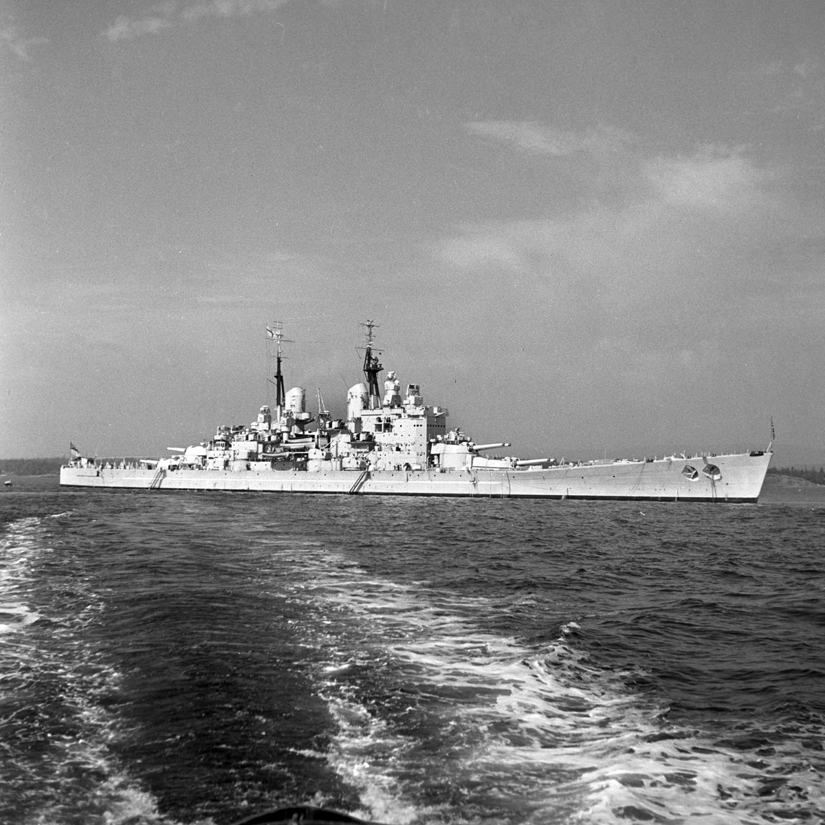 Serie. Det engelske slagskipet HMS Vanguard på flåtebesøk i Oslo. Parade med musikkorps ombord. Noen av mannskapet står med kikkerter og en pusser kanoner. Fotografert 21. juni 1954.