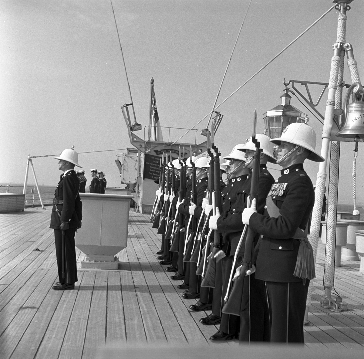Serie. Det engelske slagskipet HMS Vanguard på flåtebesøk i Oslo. Parade med musikkorps ombord. Noen av mannskapet står med kikkerter og en pusser kanoner. Fotografert 21. juni 1954.