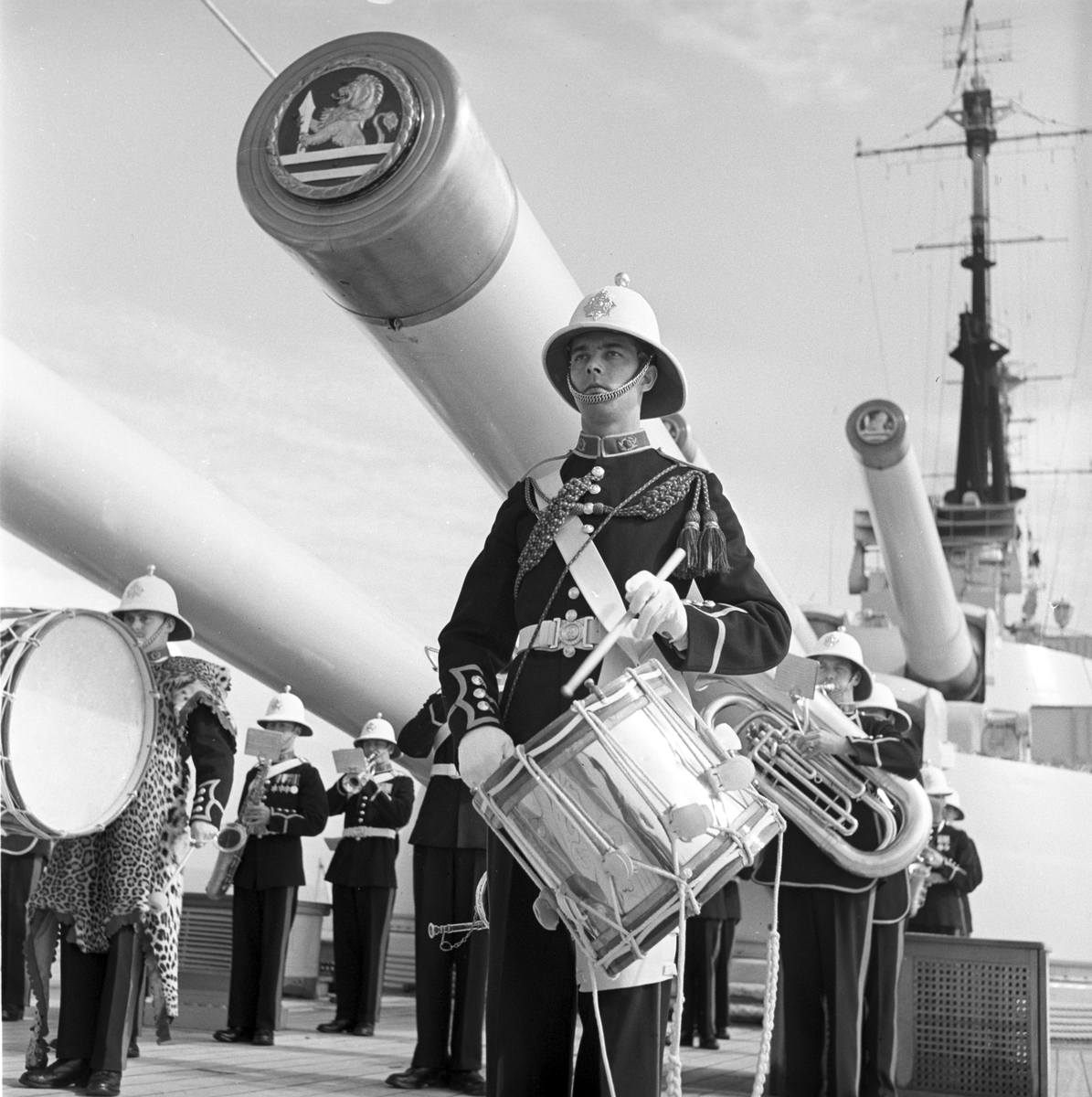 Serie. Det engelske slagskipet HMS Vanguard på flåtebesøk i Oslo. Parade med musikkorps ombord. Noen av mannskapet står med kikkerter og en pusser kanoner. Fotografert 21. juni 1954.