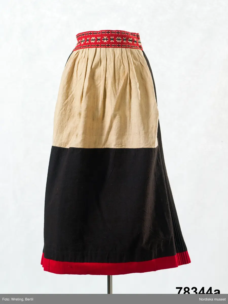 Huvudliggaren:
"Kvinnodräkt fr. Delsbo sn, Norra Helsinglands fgd, Helsingland.
a. "Ryntjeskjortel" af svart kläde med röd kant och bandväfd "kval" (linning). Kjolen "lurad"(goffrerad), skall förvaras lurad att ej vecken gå ut. 3 par fruntimmershänder hjälpas åt att "lura" den efter hvarje begagnande.
b. livstycke, rött med gröna ränder.
c. "Ryntjessärk" (rynksärk) af hvitt bomullstyg med "krus" (handbroderi) kring hals och händer.Begagnas sommartiden
d. "Bumsförkläde" af ylle, blårandigt med bandväf,"kval" i rödt och grönt.
e. "Förklesband" rödt och grönt ylle med "doppar" (tofsar) i ändarna. Lindas 1 à 2 hvarf kring lifvet och bindes framtill med stora nedhängande "locor" och ändar. Längd 262 cm, bredd 3,4 cm.
f. Kjolsäck med mässingslås och hake samt tennbroderi. Häktas under förklesbandet och hänger delvis under "försklet". Begagnas vanligen till förvaring af kyrkkryddor m.fl. kyrk-ellerkalassaker.
g. Halfhandskar af svart kläde med silkesbroderi. Begagnas sommartiden.
h. "Påshufva" hvardagsmössa af brokigt kattun. Begagnas med i nacken utslaget hår med några hårtestar hängande fritt framför öronen.
Till dräkten användes röda strumpor samt låga skor med höga klackar. Äfven kan användas silfersmycken kring halsen eller å  bröstet. En á två brokiga silkesdukar brukades omkring halsen nedstoppade under lifstycket, så att kruset kring halsen  på "ryntjessärken" sammanfästadt med ett löfspänne samt en smalare kant af hvarje sidenduk, blevo synliga. Vid handlederna sammanfästes ryntjessärken med röda sidenband eller länkknappar.

a. KJOL 
längd: 87 cm
midjeband bredd: 7 cm
av svart halvylle med svart linvarp och inslag av svart 1-tr. ullgarn, de 2 yttersta stadtrådarna är av oblekt lingarn. 4 goffrerade våder samt en slät framvåd som skarvats under förklädet med oblekt bomullslärft. 5 cm bred list av rött kläde i nederkanten runtom. Brett midjeband mönstervävt i rött och grönt ullgarn och vitt bomullsgarn. Knäppt vid framvådens vänstra sida med 2 hakar och hyskor av mässing.
b. LIVSTYCKE
längd: 39 cm
av halvylle i varptäckande kypert, varp av vitt lingarn, inslag av svart och grönt ullgarn med flaminslag av vitt, 2 fram-och sidstycken, 2 bakstycken avsmalnande till skörtveck med tre par tränsade förstärkningar av svart garn. I midjehöjd ett avsytt veck runtom, knäppt kant i kant med 8 par grova hakar och hyskor av mässing. Foder av ofärgad bomullslärft.
BE

c. ÖVERDEL
Längd: 39 cm. Längd: 58 cm - ärmlängd. Vidd: 56 cm - ärmvidd. Vidd: 114 cm. Höjd: 1,7 cm - kraghöjd. Material: Textil, bomull. Textil, linne - ärmlinning, krage. Bomullsgarn - broderi. Telnik: Tuskaft. Trådbundet broderi. Broderi, rätlinjig plattsöm. Handsömnad.
Överdel av tuskaftat vitt bomullstyg. Dubbelvikt bålstycke, isydda rektangulära halsspjäll. Täta breda stripade  rynkor mot halskrage i bomull, 1,7 cm hög. Kragen har broderier i rätlinjig plattsöm, vitt bomullsgarn över hela ytan, nuggor i kanten, langetterade bågar  i framkant. 16 cm långt sprund fram, tränsad förstärkning nedtill, 3 cm.  Vidsydd ärm med  infällda ärmspjäll, lagda veck över axeln fram och bak. Täta breda stripade rynkor mot 2,5 cm bred ärmlinning. Ärmlinningen har yttäckande vita broderier i rätlinjig plattsöm, rombiska former. Vita knytband i bomull i ärmlinningar och krage. Överdelen är handsydd.
/Inga-Lill Eliasson 2007-11-26


d. FÖRKLÄDE
längd=vådbredd: 82 cm
bredd: 97,5 cm
av halvylle, varp av svart lingarn, inslag i varptäckande kypert av svart 1-tr. ullgarn med smala ränder istarkt blått och en knappt synlig svart tråd med vita flamgarnsfläckar av bomull. Upptill stripade rynkor där de blå bårderna utnyttjats dekorativt i rynkningen. Mönstervävt midjeband i grönt på rött ullgarn , bandet knäpps med 2 hakar och hyskor i vänster sida.
I nederkantens båda hörn infodringar på insidan av svart bomullslärft, för att tyget inte skall rulla sig.



Berit Eldvik 2004