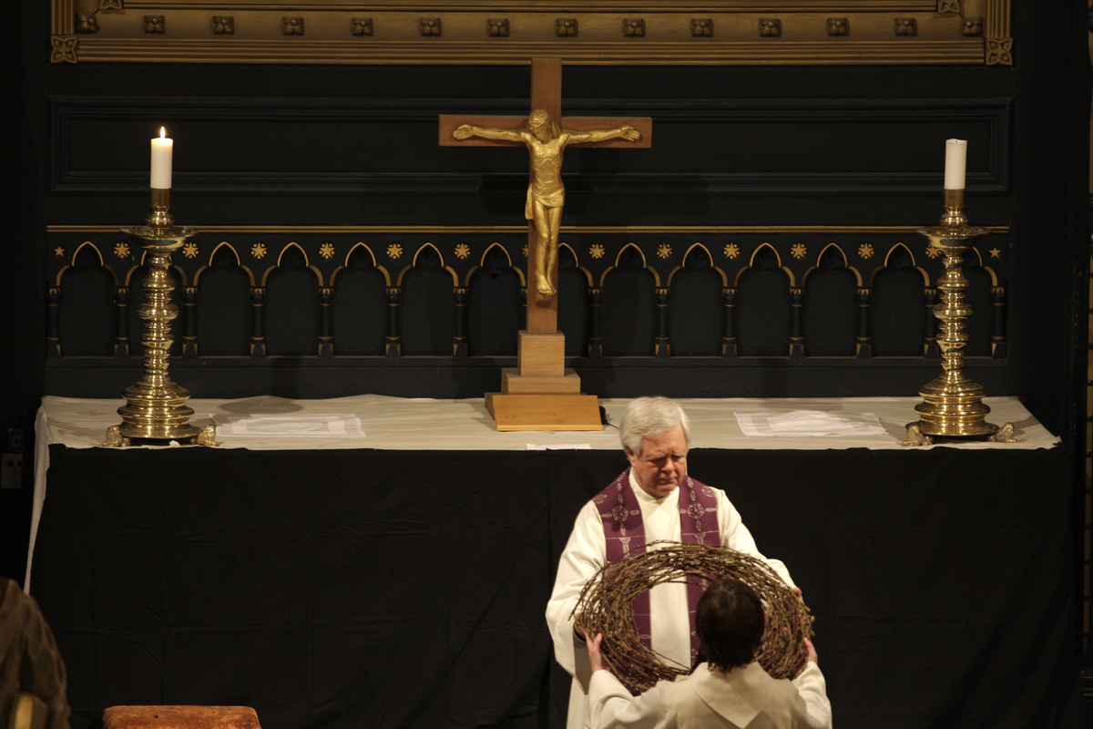 Kristiansand Domkirke, skjærtorsdag, 20.03.2008. Prest Helge Schmidt kledd i hvit alba og lilla stola tar i mot tornekransen som skal legges på alteret hvor kun ett lys brenner. Alteret er dekket med svart stoff (antependium).   Krusifiks. Kirketekstilene er utført av Borgny Farstad Svalastog.