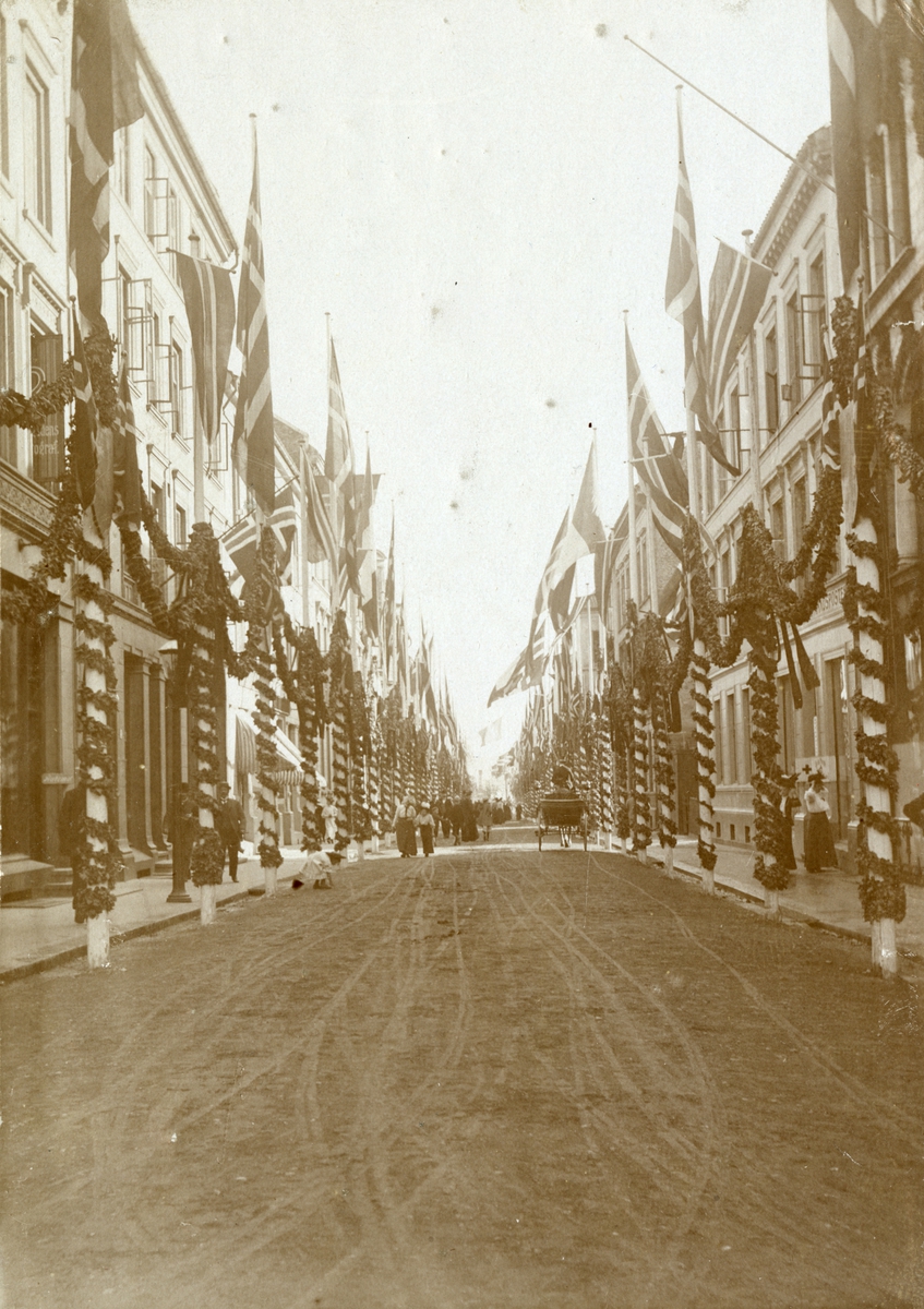 Serie med fire foto fra den franske prsidenten Clement Armand Fallières statsbesøk i Kristiania i 1908. Velkomstpaviljong med baldakin, pyntet med girlander og flagg. Dekorasjoner utført av B. Lange, antakelig. Tilskuere på Honnørbrygga i hovedstaden. Karl Johans gate er også pynytet med dekorasjoner.