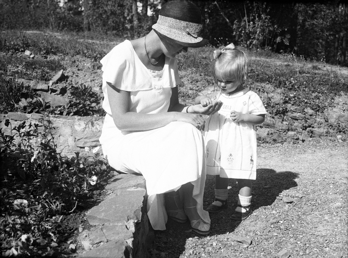 Siri står i hagen og plukker noe fra sin mor Dordi Arentz hånd. Fotografert 1932.