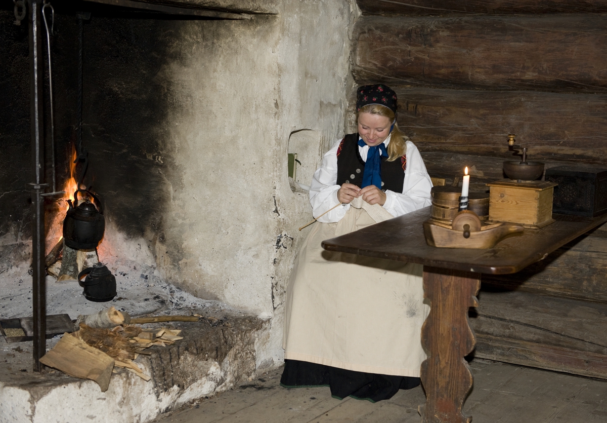 Stue fra Grøsli, Flesberg. Numedalstunet på Norsk Folkemuseum, august 2010. Formidling i friluftsmuseet. Tunvert strikker og koker kaffe ved peisen i "Grøslistua".