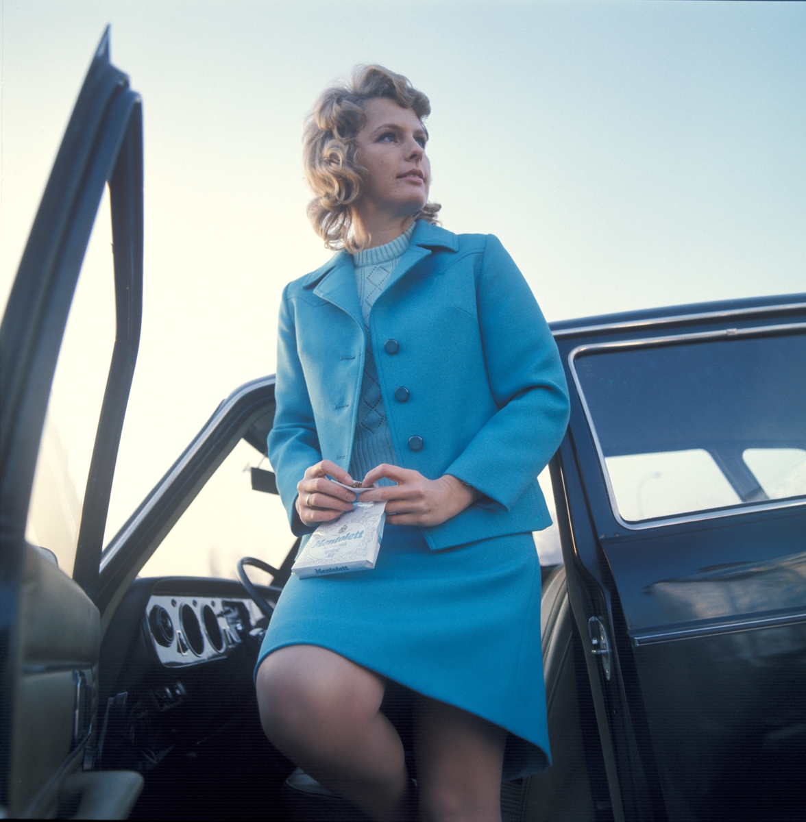 Reklamefoto. Kvinnelig modell i bil ruller seg en sigarett.
