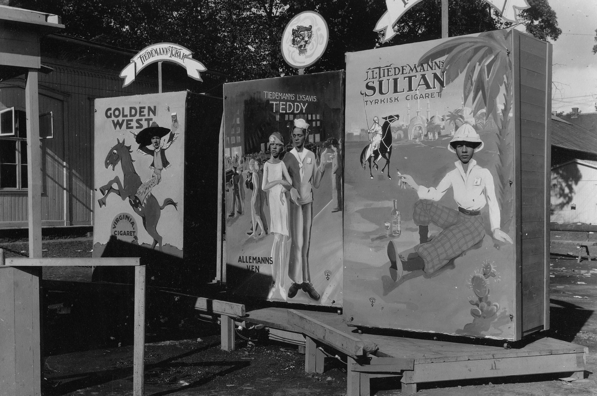 Foto fra Tiedemanns stand på en messe i 1926 hvor publikum kunne bli gratis portrettert med sitt ansikt kikkende gjennom en av Tiedemanns reklameplakater.