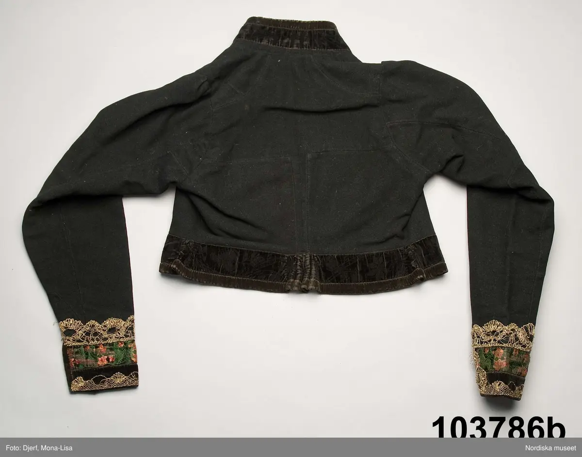 b. Brudtröja av svart vadmal,  Runt alla kanter bård av ytterst brunsvart sammetsband och innanför ett 4 cm brett svart sammetsband  med invävt bladmönster. På ärmarna ett svart slätt sammetsband med pålagd guldspets därefter siden band i rosa och grönt på botten av  svart  sammet och överst i bården en knypplad guldspets. 
c: Förkläde. Material: Textil, bomull. Teknik: Manufakturvävning. Handsömnad. Längd: 77 cm. Bredd: 110 cm. Färg: Vit.
Förkläde i vitt manufakturvävt bomullstyg, ihopsytt i mitten, smalrandigt, stärkt. Rynkningar mot midjelinning i tuskaftat bomullstyg, 1,5 cm bred, fastsydda bomullsband i sidorna. Uppvikt fåll nedtill, 6,5 cm, ovanför fåll, 5 lagda veck med ca 1 cm mellanrum, enkel utdragssöm i kanten av vecken.
/Inga-Lill Eliasson 2008-02-25

e: Krage. Längd: 47,5, cm - totallängd, bröststycke. Bredd: 33 cm - bröststycke. Höjd: 14 cm - kraghöjd, inkl spets. Material: Textil, bomull. Lingarn - spets. Bomullsgarn - broderi. Teknik: Tuskaft. Vitbroderi, Knyppling. Handsömnad.
Krage i tuskaftat vitt bomullstyg. Rektangulär duk, uppklippt halshål med fastsydd krage, 14 cm hög. Kragen har 3,5 cm bred fåll, enkel utdragssöm i kanten. Vitbroderi  i framkant,  plattsöm och kantsydda hål med infällt tyll, två sydda knapphål. Handknypplad spets fastsydd på långsida och korstsidor, 2,5 cm bred. Öppning fram, 24 cm långt sprund. Kragen är handsydd.
Lästips: Svensson Sigfrid, (1935). Skånes Folkdräkter, en dräkthistorisk undersökning 1500 - 1900. Stockholm: Nordiska Museets Handlingar: 3.
/Inga-Lill Eliasson 2008-02-19