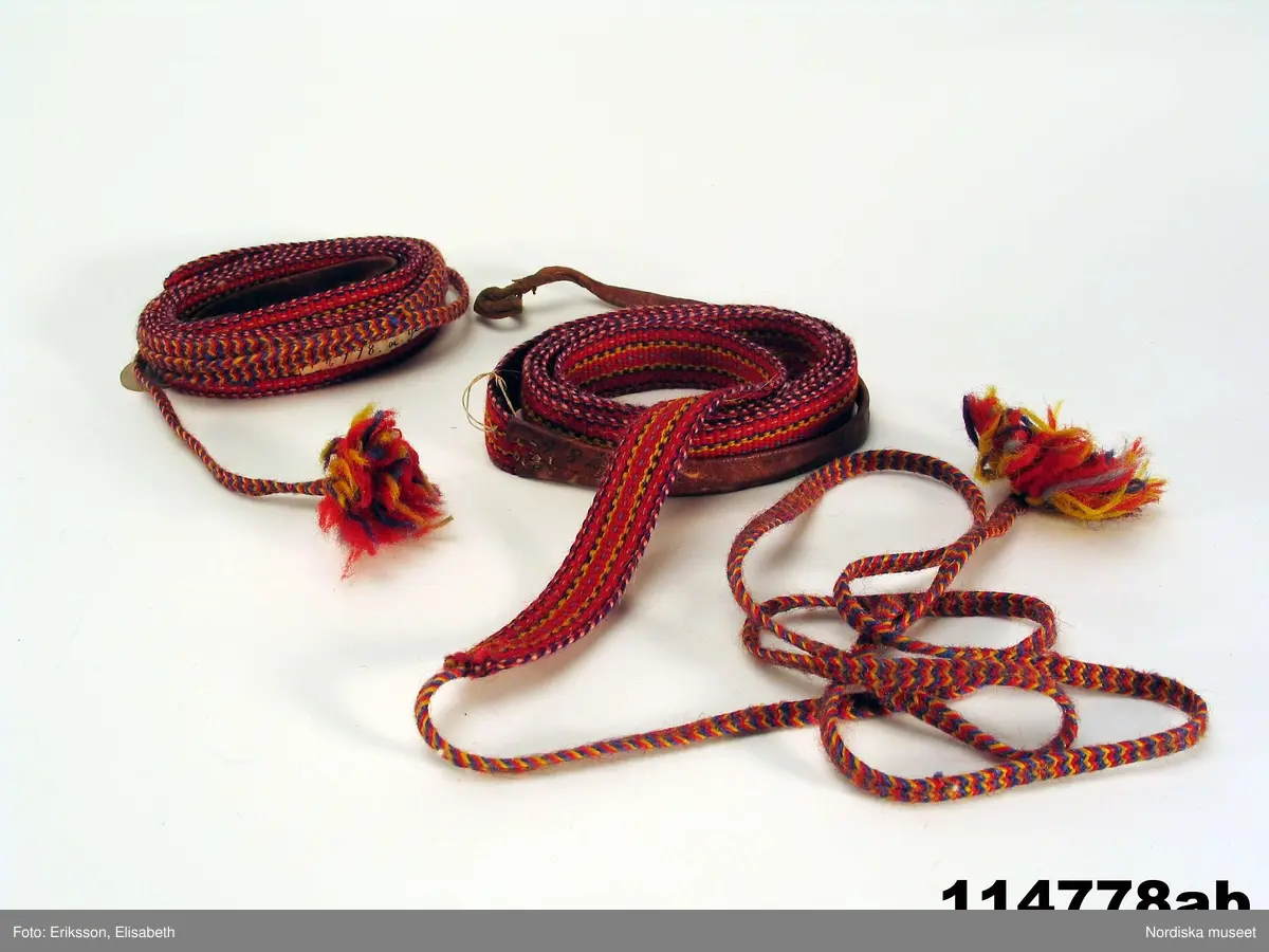 Huvudliggaren:
"a-b  1 par skoband för man, dels vävda, dels flätade av mångfärgat ullgarn. Från Kalasvuoma lappby. Ink. 2/2 1910 [från] Hallström G., amanuens, Stockholm jämte 114.773 - 114.783 [...]. [Brukningsort:] Lappland Torne lpmk Juckasjärvi sn."