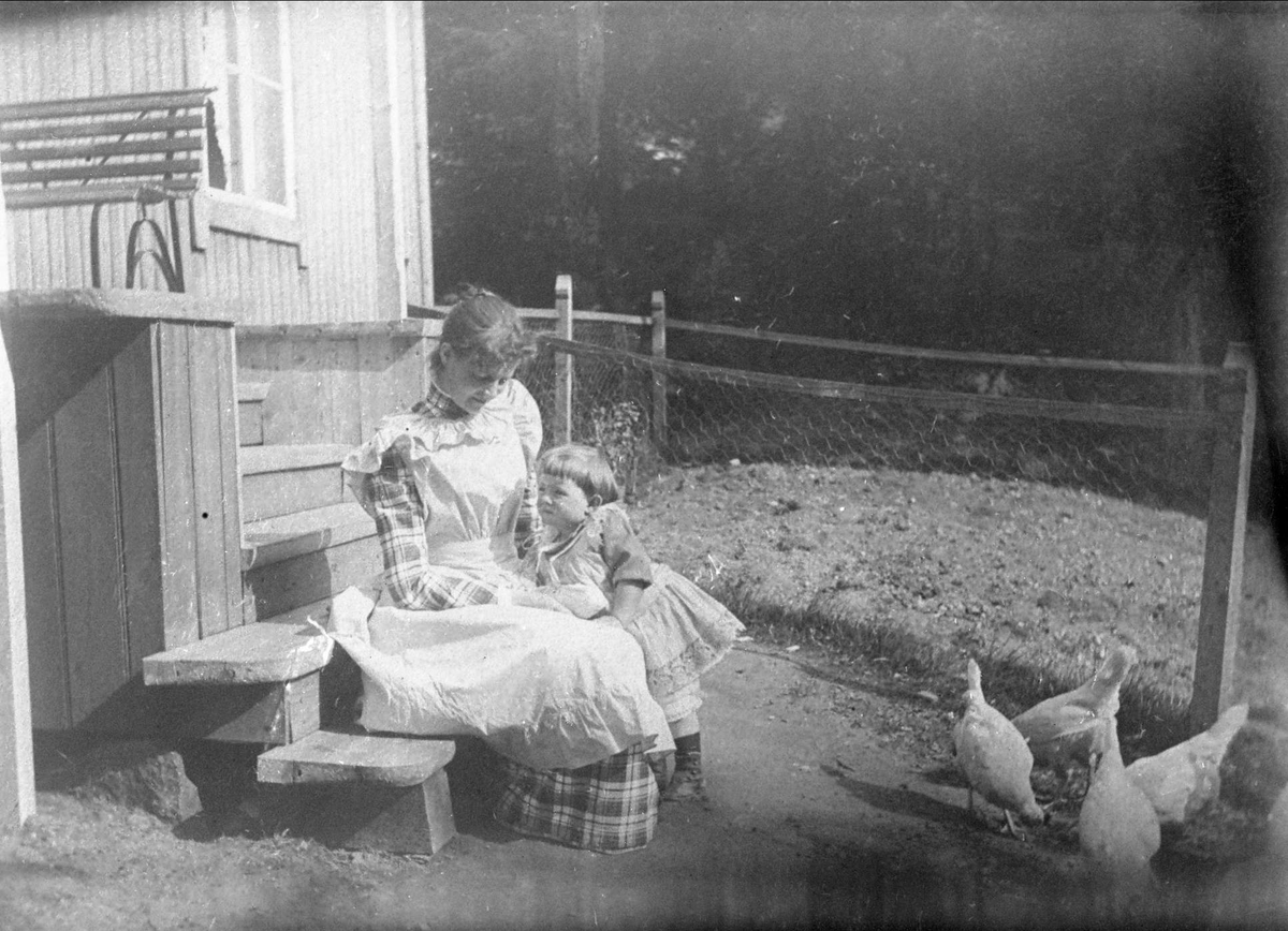 Avfotografering. Kvinne og barn sitter på trapp med høner spaserende i forkant. Fru Doktor Fricks kopi.