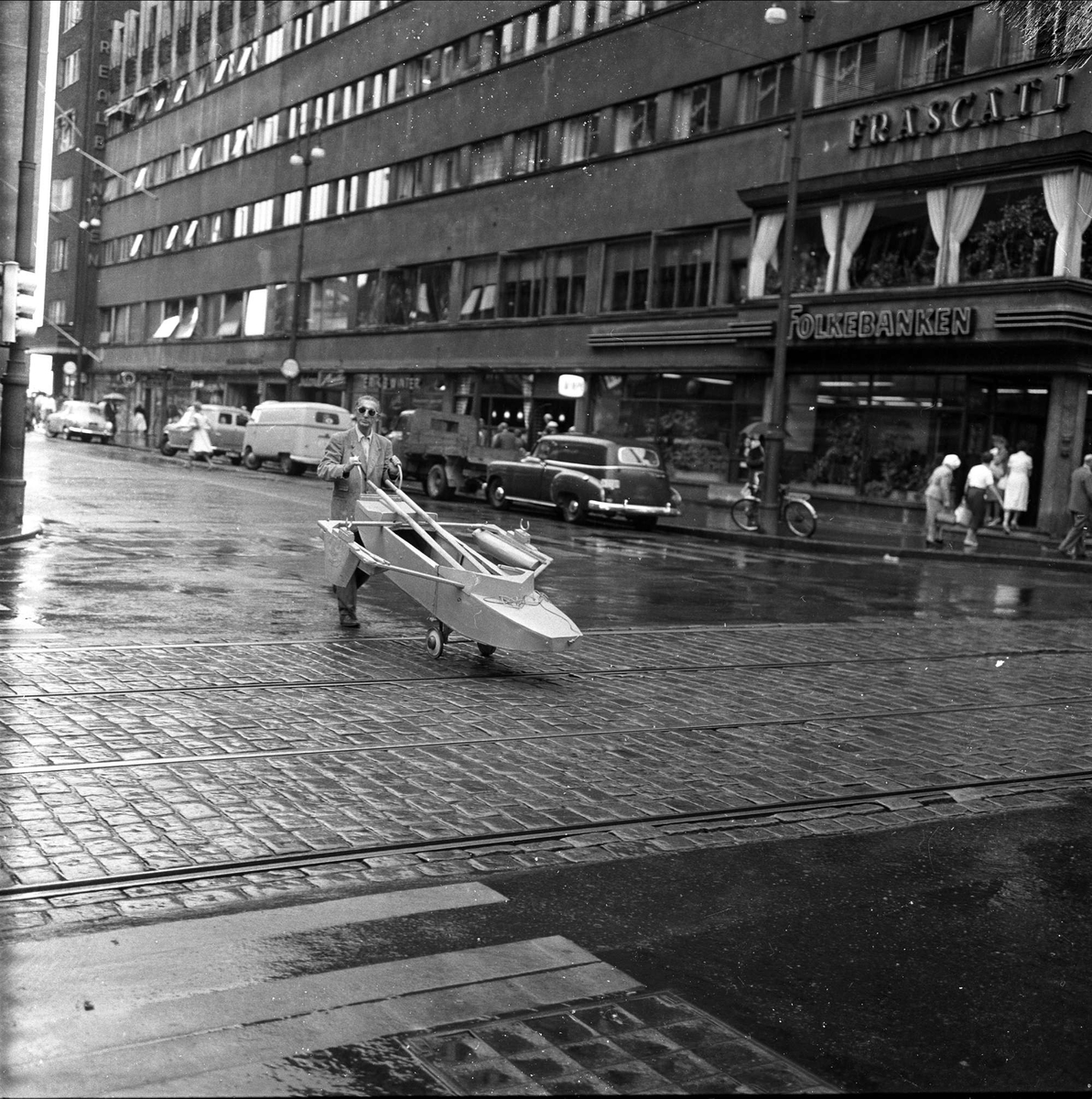 Krysset Roald Amundsens gate og Stortingsgaten. Restaurant Frascati bak til høyre. Gatebilde med person som triller robåt. Oslo juli 1959.