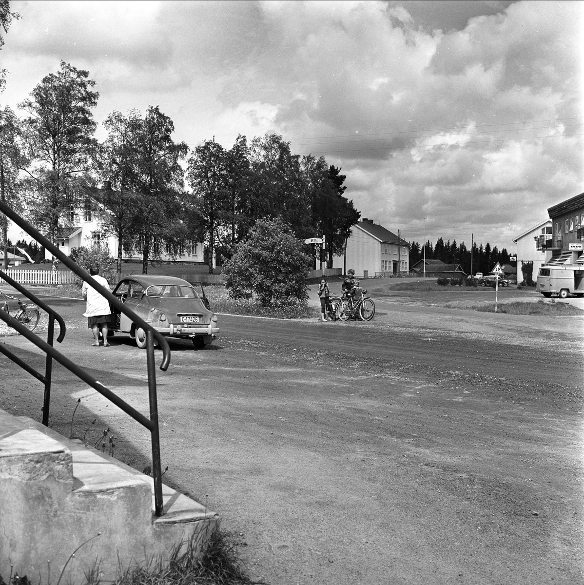 Sammenslåing av Aurskog og nabokommune. Aurskog, januar 1964. Åpen plass med bil og sykler.