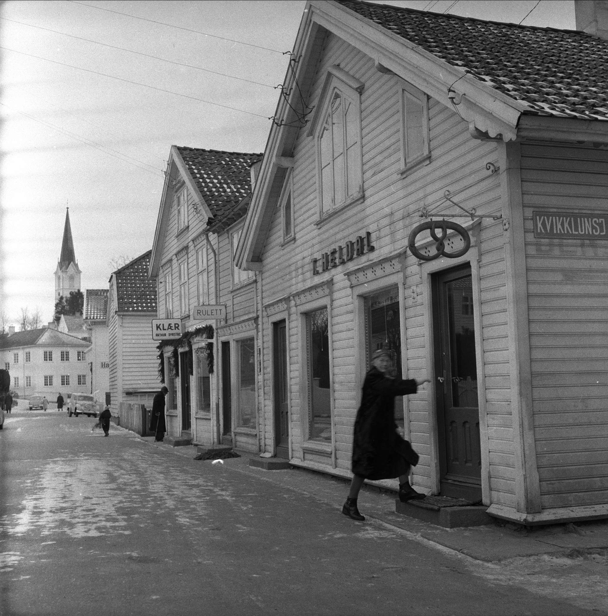 Glimt fra Lillesand, desember 1957. Folk og forretninger i gate.