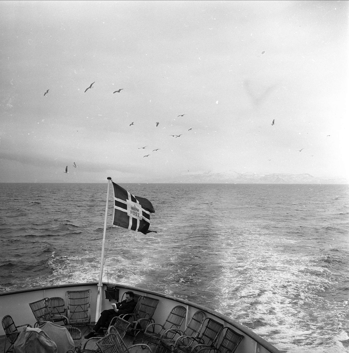 Nord-Norge, april 1963. Fra Hurtigruta, passasjerer på dekk og postflagg.