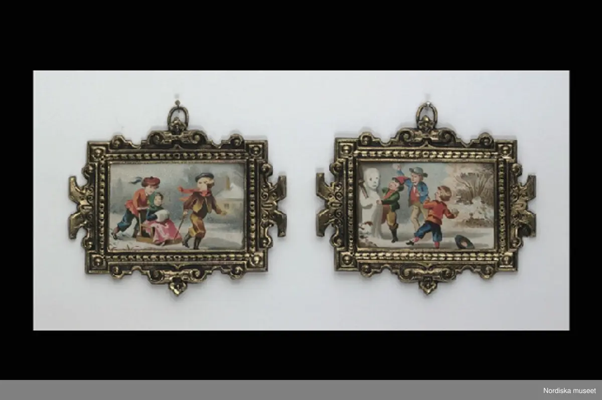 Inventering Sesam 1996-1999:
L  6,2   B 5 (cm)
Tavla, ett par (a,b), till dockskåp, färgtryck på papper, vintermotiv av a) två gossar som drar flicka i släde, b) tre gossar som tillverkar en snögubbe. Rektangulär ram av mönsterpressad gulmetall med reliefdekor, ring för upphängning.
Tillhör dockskåp från omkr 1840, inv nr 145.505, inrett 1872 av leksakshandlare W A Bandel, Västerlånggatan, Stockholm, för dottern Thyra, vilken vid överlämnandet till museet själv gjort uppställningen av föremålen i dockskåpet. 
Anna Womack dec 1997