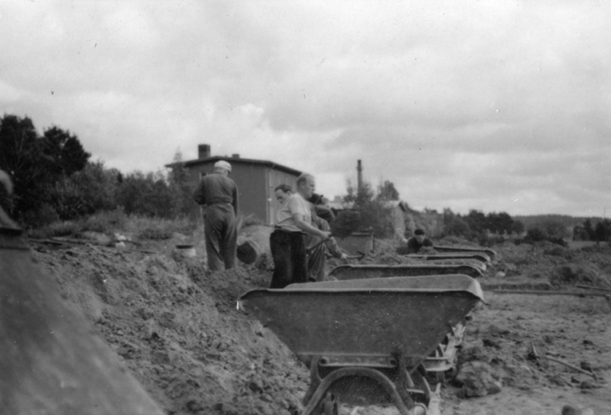 Idrottsplatsen på F 2 Roslagens flygflottilj byggs, 1943. Civilanställda tjänstemän i arbete med grävning. Människor och maskiner i arbete med grävning.
