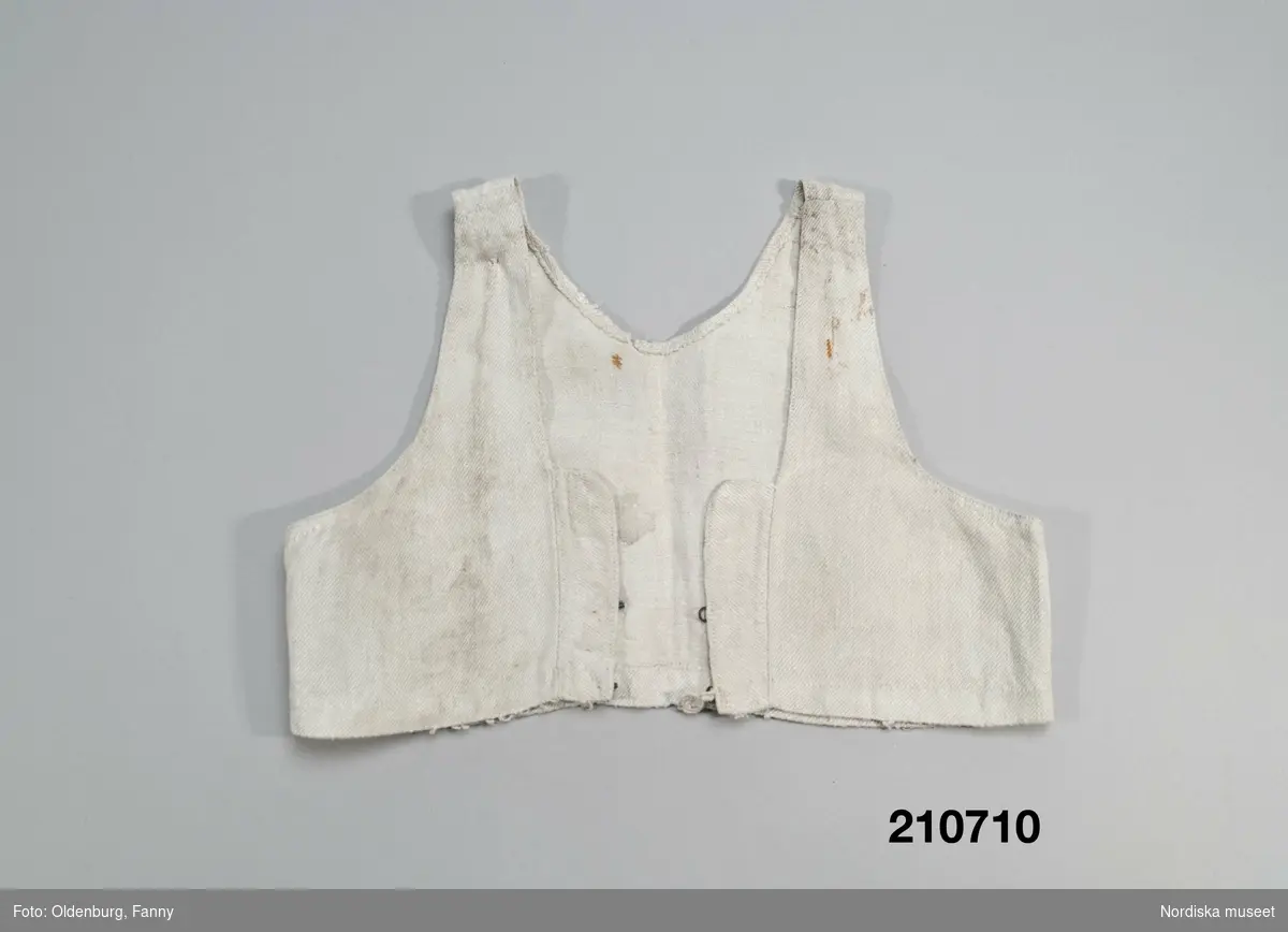 Livstycke, "bod" som varit fastsydd på en linnekjol. Av handspunnet lingarn, blångarn, i treskaftad kypert, "treskäft".  2 raka framstycken och ett ryggstycke, skarvat på axlarna. 3 påsydda band i ryggen som sömmarkeringar, blå med plockat mönster i vitt lingarn. Öppet framtill med 3 cm breda knäppkanter på båda sidorna med 2 par hakar och hyskor av mässing. Fåll nedtill med stygnrester av lingarn där den varit fastsydd mot kjolen.
Anm. sliten med fläckar och ett hål i ryggen.
Denna typ av livkjol, kallas i Mora och på Sollerön för vitsärk och användes sommartid. De kunde vävas mer eller mindre grova, och syddes mer eller mindre fint, släta, grovrynkade eller finrynkade och med grövre eller finare liv (bod) alltefter som man avsåg dem till grövsta vardagsbruk eller till helgdagsplagg.
Till fint hade de ofta liv av blommigt tyg men även röda eller gröna vadmalsliv förekom, de enklare hade vitt linneliv med bandgarnering. 
Vitsärkarna kom rätt tidigt ur bruk, sist var det de gamla gummorna, som nyttjade dem. Få är bevarade, ty det var vanligt att kvinnorna sveptes i dem.
Se Ella Odstedt: Folkdräkter i övre Dalarne sid 194-195.

Jfr. hel livkjol från Sollerön inv.nr 211804.
/Berit Eldvik 2007-09-21