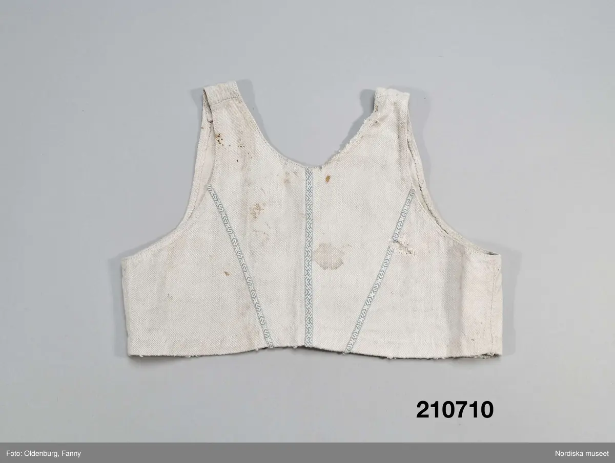 Livstycke, "bod" som varit fastsydd på en linnekjol. Av handspunnet lingarn, blångarn, i treskaftad kypert, "treskäft".  2 raka framstycken och ett ryggstycke, skarvat på axlarna. 3 påsydda band i ryggen som sömmarkeringar, blå med plockat mönster i vitt lingarn. Öppet framtill med 3 cm breda knäppkanter på båda sidorna med 2 par hakar och hyskor av mässing. Fåll nedtill med stygnrester av lingarn där den varit fastsydd mot kjolen.
Anm. sliten med fläckar och ett hål i ryggen.
Denna typ av livkjol, kallas i Mora och på Sollerön för vitsärk och användes sommartid. De kunde vävas mer eller mindre grova, och syddes mer eller mindre fint, släta, grovrynkade eller finrynkade och med grövre eller finare liv (bod) alltefter som man avsåg dem till grövsta vardagsbruk eller till helgdagsplagg.
Till fint hade de ofta liv av blommigt tyg men även röda eller gröna vadmalsliv förekom, de enklare hade vitt linneliv med bandgarnering. 
Vitsärkarna kom rätt tidigt ur bruk, sist var det de gamla gummorna, som nyttjade dem. Få är bevarade, ty det var vanligt att kvinnorna sveptes i dem.
Se Ella Odstedt: Folkdräkter i övre Dalarne sid 194-195.

Jfr. hel livkjol från Sollerön inv.nr 211804.
/Berit Eldvik 2007-09-21