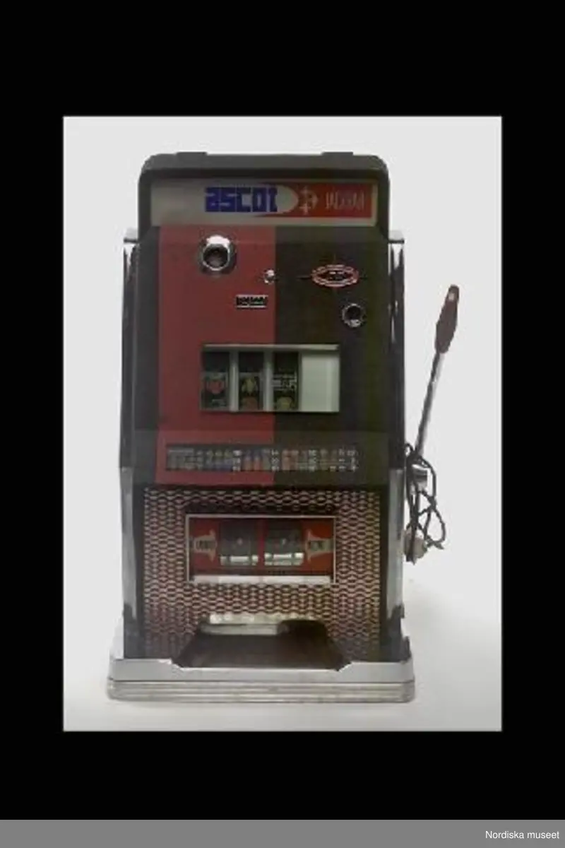 Inventering Sesam 1996-1999:
L 46 cm
B 44,5 cm
H 74 cm
Spelautomat, enarmad bandit. Hölje av svart och röd metall och svartvit perstorpsplatta. Stående på träplatta med vitmetall. Framtill olika skyltar bakom tjockt glas. Mitt på (eg. innuti) tre rullar med olika symboler, t ex apelsiner, halva meloner, siffror mm, bakom glas. På vänster sida hål för mynt. På höger sida en arm med rött handtag av backelit. På vänster sida elektrisk sladd med vit kontakt. 
Text på skyltarna text "ASCOTT JACKPOTT", "Reject", Jackpott" och karta med de olika symbolkombinationer som man vinner på.
Innuti mekanism av metall. Öppningsbart bakstycke (med nyckel vilken saknas vid inv. 1998) 
Liten svart skylt nertill på vänster sida; "Ascott s.p.a. / Calenzo - Florence Italy / Tipo 88 / M.la 067"
Funktion; man stoppar in ett mynt (troligen 1 krona) och drar i armen. Rullarna med de olika symbolerna surrar och stannar sedan en och en (går ev att själv stoppa med en liten knapp mitt på framsidan). Om man lyckas få någon av de kombinationer som finns på skylten så vinner man pengar, som kommer ut längst ned. Mest vinner man om man får tre lika symboler. Enarmade banditer har varit vanliga på motell, konditorier, bensinstationer och dyl. 1973 fanns ca 140 000 spelautomater, samma år infördes skatt på automaterna. Senare blev de förbjudna. 
Jmfr liknande enarmad bandit av samma tillverkare (?) inv.nr 287.426
Bilaga
Leif Wallin feb 1998