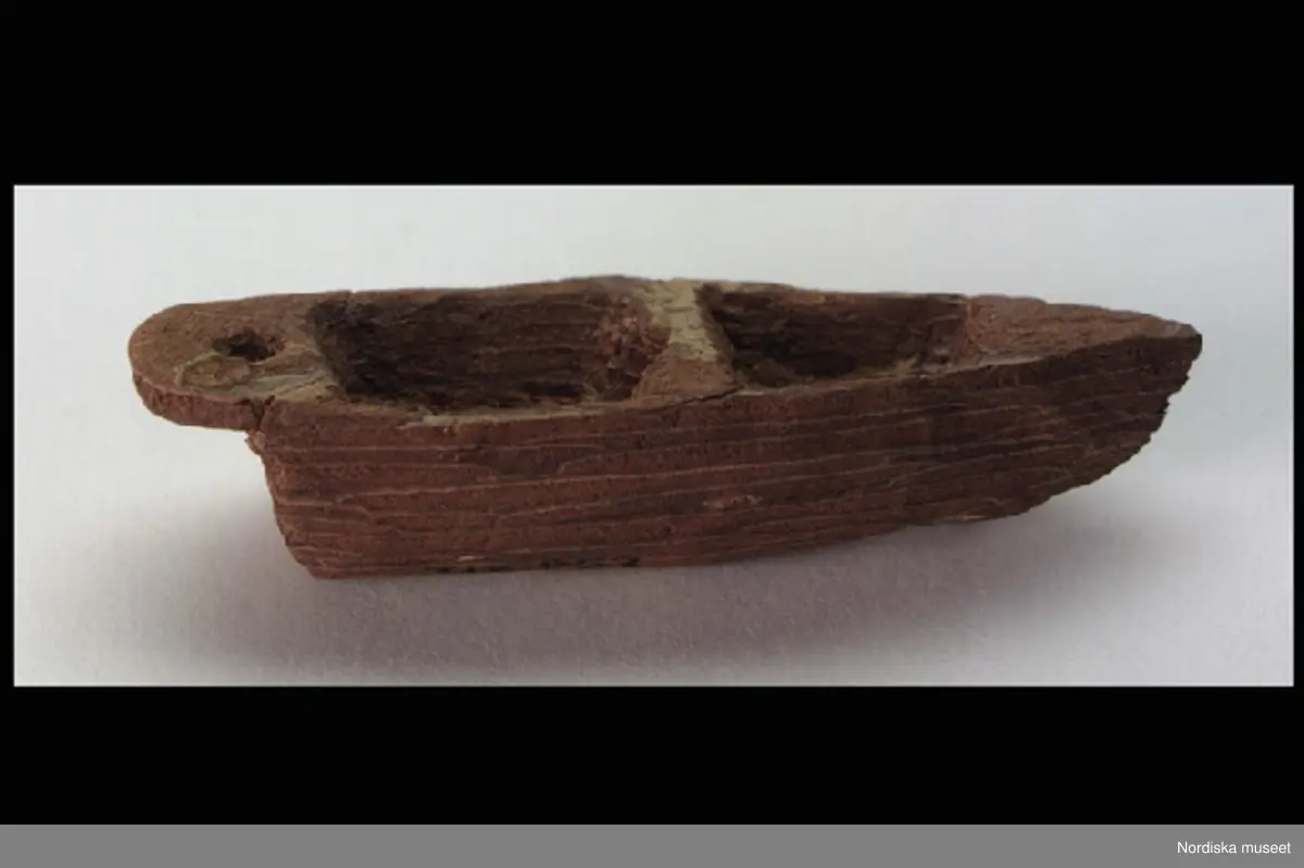 Inventering Sesam 1996-1999:
H 1,7 cm
L 7 cm
B 2,5 cm
Leksaksbåt täljd av tallbark. Spetsig för, rundad akter. Inredd med två sittbrunnar och masthål. Rundad botten.
Har täljts av Gunnar Hazelius (1874-1905, son till Skansens och Nordiska museets grundare Arthur Hazelius).
Bilaga
AT 1987 [=Annika Tyrfelt]