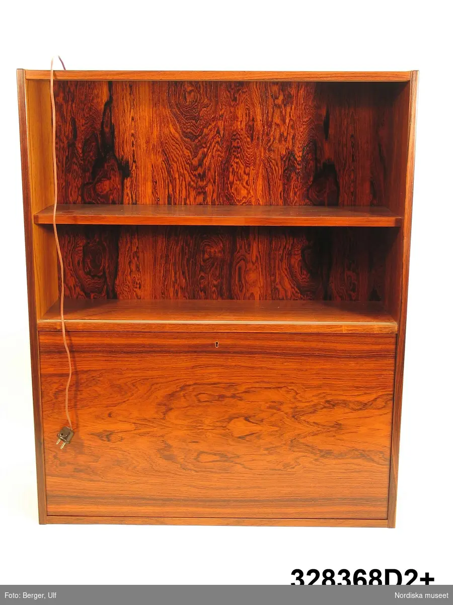 a-e:
Bokhylla, "Excellent",  med TV-bänk samt bar- och vitrinskåp, jakarandafaner på spånskiva, IKEA, 1968. 

Hyllan består av fyra sektioner med hyllor löst placerade på underredet. Skåp- och byråunderdelar med ryggar av masonit, fastnitade. Kvadratiska ben, fastskruvade i underredet. Lådsidor m.m. av björk och lådbottnar av vitlackerad masonit. Flyttbara hyllplan. Draghandtag och gångjärn av mässing.  Enligt IKEA-katalogen 1968 är ytan plastbehandlad.

Hyllan uppställd, från vänster till höger:
a:1+) Skåp med två dörrar samt a:2+) hyllöverdel, ett fast och två flyttbara hyllplan. Överst vitrindel med två skjutdörrar av glas (höjd 53,5 cm, bredd 41,5 cm).
b:1+) Byrå med tre lådor samt b:2+) hyllöverdel med tre flyttbara hyllplan. 
c:1+) Tv-bänk med en låda samt c:2+) hyllöverdel med tre flyttbara hyllplan.
d:1+) Skåp med två dörrar samt d:2+) hyllöverdel med 1 flyttbart hyllplan. Överst vitrindel med två skjutdörrar av glas (höjd 53,5 cm, bredd 41,5 cm), därunder ett barskåp med spegel som bakvägg, utrymme för flaskor till vänster och två glashyllor (48 x 19,5 cm) till höger. Barskåpet med fällbar klaff med lås. Belysning monterad i skåpets överkant.
e) Nyckel till barskåpets klaff. L 4,3 cm.

Möbeln har använts av givarinnan, Berith Helldén, f. 1945, hemmafru, och hennes man, Lars-Göran Helldén, f. 1946, inköpare, Tungelsta. Paret gifte sig 1967 och bodde som nygifta i en liten lägenhet i Borås. När de fick möjlighet att flytta till en större lägenhet i samma stad, utökades vardagsrumsmöblemanget. Hyllan inköptes 1968 på IKEA i Älmhult. Enligt IKEA-katalogen 1968 kostade de fyra hyllsektionerna totalt 2484 kronor. Hyllan har använts som förvaringsmöbel i vardagsrummet i Borås och i familjens nuvarande bostad i Tungelsta fram till våren 2005, då den inköptes av museet.

Hyllans innehåll har dokumenterats och en utförlig intervju med Berith Helldén har gjorts 2005-05-09 (se arkivreferens).
/Anna Womack 2005-10-18
