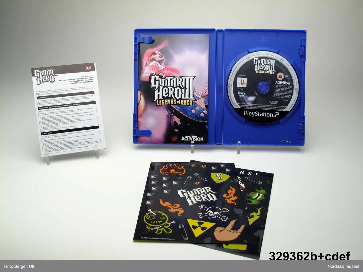 TV-spelet "Guitar Hero III Legends of Rock" med förpackning. 
a+) Elgitarr med avtagbar hals, av svart plast, svart axelrem av syntettextil med konstläder (plast) och plastöglor.
b+) 2 ark med klisterbilder att fästa på gitarren
c) Broschyr med instruktioner om funktion och säkerhet på flera olika språk.
d) Fodral av blå plast med inplastat omslag av papper med text. På framsidan "Playstation 2 / Guitarr Hero III LEGENDS of ROCK" och bild på hårdrockare. Baksidan bl.a. "SLÄPP LOSS DIN INRE ROCKLEGEND / Över 70 rockiga låtar.".
e) CD-skiva med programvara (förvarad i fodral d).
f) Instruktionsbok på de nordiska spårken (förvarad i fodral d) 
g+) Förpackning av papp. Ytterfodral med text och bilder. Inre lådan med inredning för de olika delarna.
 
Tv-spelet är avsett för spelplattformen Playstation 2, vilket är en vanlig spelplattform. Spelet går ut på att det spelas upp en låt (man väljer själv låt och nivå) och ska sedan försöka spela på gitarren genom att trycka på knapparna och på så vis lyckas spela samma ton som musiken spelar samtidigt.

Vid förvärvet avlägsnades plastpåsar som del av a och b låg i, samt två 1.5volts-batterier av märket Duracell som låg i gitarren, då de ej bedömdes möjliga att spara. Även fyra papperspåsar med Silicagel (för att hindra att fukt skadar elektronik mm) togs bort.

Nyinköp den 2008-02-20 för att rekonstruera julkklappsönskemål julen 2007 från Erik Thomelius född 1999, Vaxholm. Inköpt av Nordiska museet för 439 kr. Ingår i projektet "Barn tar plats". Se dokumentation i arkivet D455.
/Ulf Hamilton 2008-05-27     