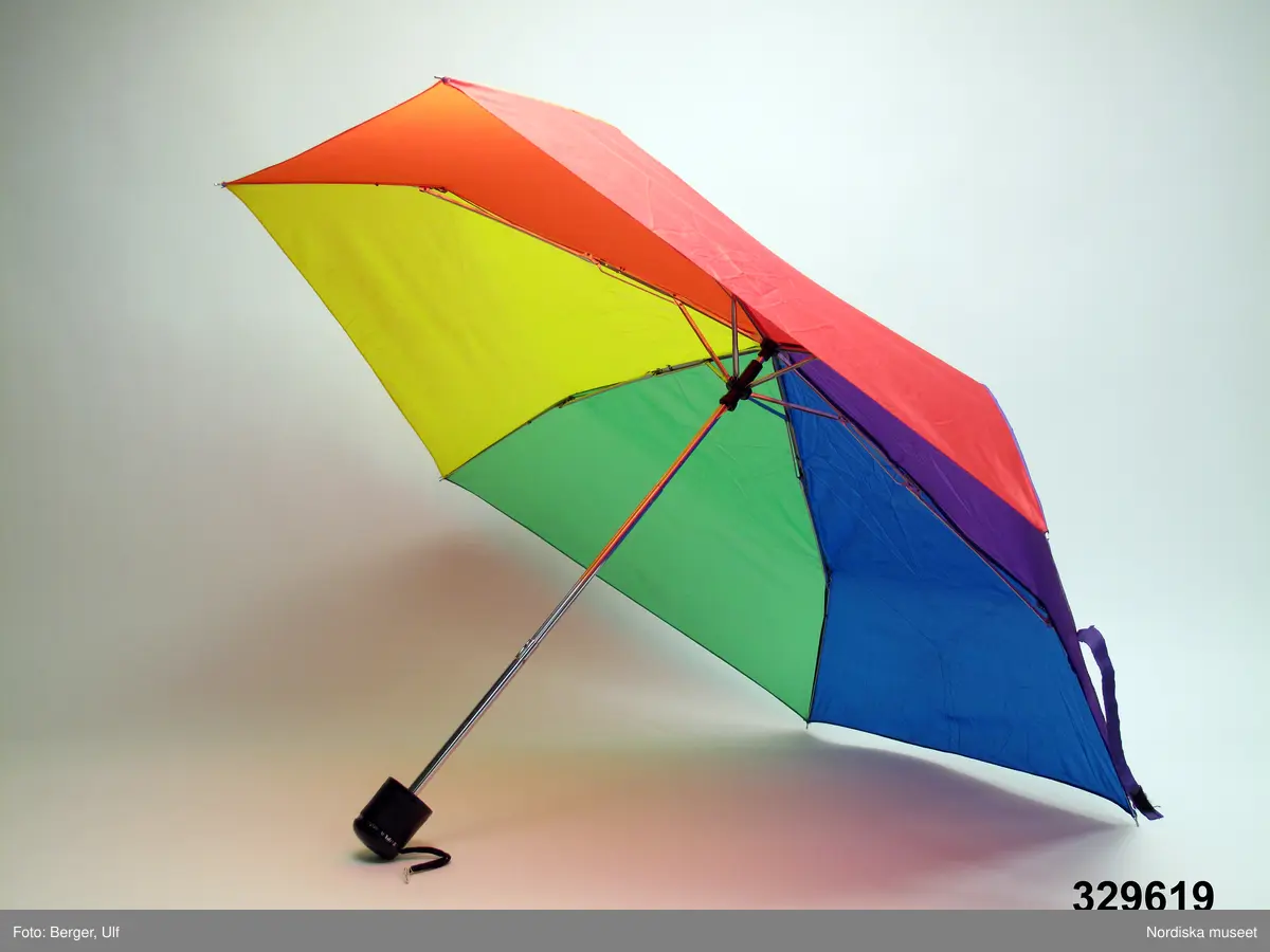 Paraply med svart plasthandtag med svart snodd i konstmaterial. Ställningen i vitmetall. Paraplytyget av nylon i olika tårtbitsformade fält i färgerna blått, lila, två nyanser rött, gult och grönt. På handtaget påklistrad etikett med texten "SUPER-MINI". Litet band av nylon fäst på det lila fältet. Bandet, som är försett med kardborreband, sätts runt paraplyet i ihopfällt tillstånd för att hålla tyget på plats. 

Paraplyet köptes av givaren och hans pojkvän under Stockholm Pride / EuroPride 2008 vilket är den största årliga festivalen för HBT-personer i Sverige och 2008 firades 25 juli-3 augusti.

Utdrag ur intervju med givaren: De köpte tre likadana paraplyer i QX shop i Pride Park. Pojkvännen tyckte att de kunde vara bra att ha i den stora paraden på lördagen som de deltog i. Det regnade en del under de sista dagarna under Prideveckan och speciellt på lördagen innan och under paraden. Ett regnbågsfärgat paraply tyckte de var bra då det tydligare visar att man är en HBT-person. Veckobandet och dogtagen syns ju inte på lite längre avstånd. Givaren tror att paraplyerna kostade 99kr/st vilket han tycker är ganska mycket för ett så litet och enkelt paraply och då liknande paraplyer brukar kosta mindre. Men eftersom det var regnbågsfärgat så tyckte han det var värt det i alla fall. 
De hade tänkt använda paraplyerna som vanliga paraplyer efter Prideveckan, men ett har de lånat ut och inte fått tillbaka, och ett har redan gått sönder och det tredje är detta som museet får. 

Givaren och hans pojkvän, som har varit på de flesta Pride-firanden sedan 1998 och de brukar försöka gå på så mycket av aktiviteterna som möjligt under veckan. Se vidare intervju med givaren om hans pridefirande i arkivet (D.457).

Föremålet ingår i Nordiska museets dokumentation av Europride 2008 med föremål, intervjuer och fotografier. Se arkivet D.457. Övriga föremål med anknytning till Peter Csaszti se inv.nr 329.615-329.620 samt 329.669-329.670.
/Leif Wallin 2009-03-06