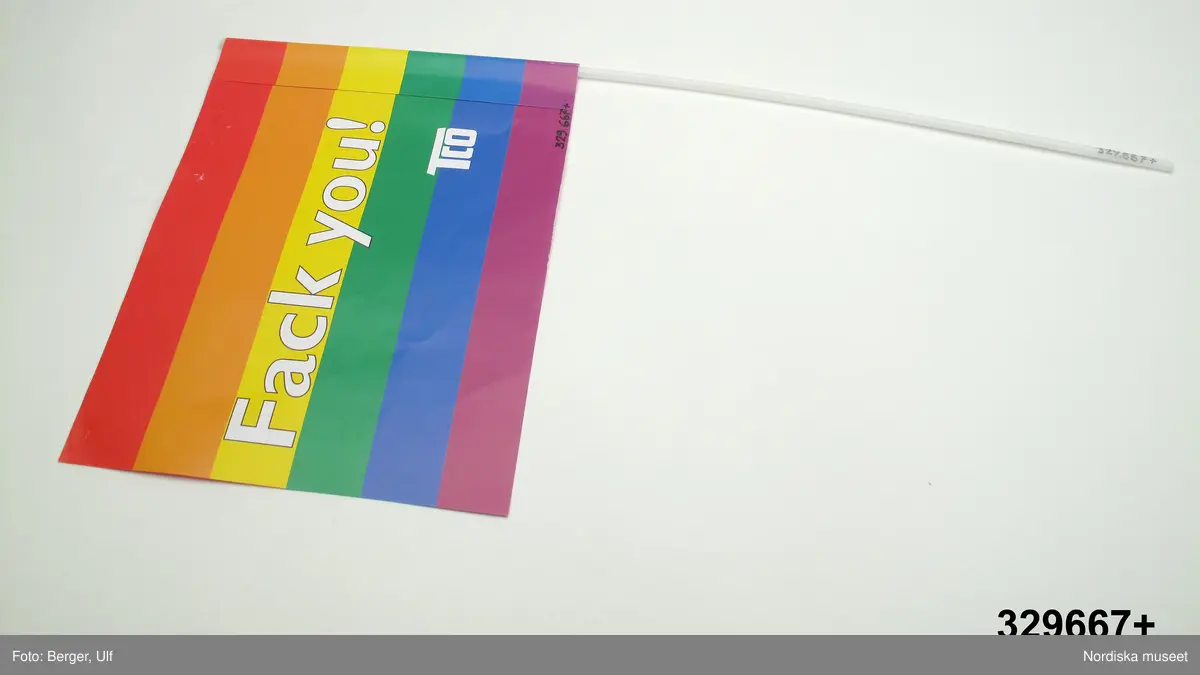 Flagga med pinne. Flaggan av papper med tryck. På framsidan text "Fack you / TCO" mot bakgrund av horisontala ränder i färgerna (uppifrån och ner) rött, orange, gult, grönt, blått och lila, de s.k. regnbågsfärgerna. Flaggan är i ena änden klistrad så att en kanal bildas där en pinne av vit, ihålig plast, skjuts in. 

Färgerna är de s.k. regnbågsfärgerna som ingår i regnbågsflaggan, som ofta används som symbol för HBT-tillhörighet. Även flaggans rosa baksida ska syfta på HBT-tillhörighet då den rosa färgen också ofta används som symbol för just detta.

Flaggan ingår i Nordiska museets dokumentation av Stockholm Pride / Europride 2008. Stockholm Pride är den största årliga festivalen för HBT-personer i Sverige och som 2008 firades 25 jul.-3 aug. Detta år var Stockholm Pride även värd för Europride. Pridefirandet är framför allt uppdelat på två platser, Pride House (år 2008 i Kulturhuset) och Pride Park (i Tantolunden). Flaggan delades ut av TCO (Tjänstemännens centralorganisation)  i de tält de delade med Socialdemokraterna i Pride Park. 

Flaggan är ett exempel på hur många företag och organisationer anpassar sina marknadsföreingsprodukter efter vilka man riktar sig till. "Fack you" ska ge associationer till Fuck You, och sådana tvetydiga syftningar på sex är inte ovanliga när man vänder sig till HBT-personer. 

Föremålet ingår i Nordiska museet dokumentation av Europride/Stockholm Pride 2008 med intervjuer, fotografier och föremål. Se vidare arkivet (D.457).
/Leif Wallin 2009-05-14