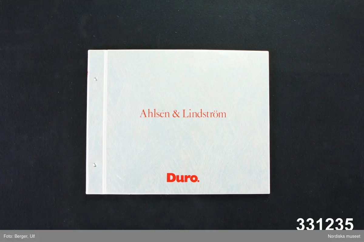 Tapetprovbok, gråmelerade pärmar av papp klädda med plast. Text på framsidan "Ahlsén & Lindström / Duro,". Samma text på ryggen. På den vita baksidan "Duro. MADE BY DURO SWEDEN AB". På första sidan bild på fyra personer i tapetfabrik samt text: "Ahlsén & Lindström / Gamla nordiska traditioner inom måleriteknik coh limtrycksförfarande har inspirerat oss vid utformningen  av denna kollektion. Vår ambition har varit att återskapa en hantverkskänsla i industriell tillämpning. En förutsättning för detta har varit desl Duros speciella limtrycksteknik med rejäla färgmängder i trycket, dels det hantverksmässiga sättet att arbeta fram kollektionen i nära samarbete med färgmästare, mönsterteknniker och tryckmästare. Tapeterna är gjorda för att passa såväl hemmiljö som offentliga rum och olika arbetsmiljöer. Därför finns också ljusreflexionsvärden uppmätta. Kollektionen har utformats med en viss gemensam grundkaraktär. Avsikten är att olika rum skall kunna kombineras med varandra på ett variationsrikt sätt men ändå ge en sammanhängande helhetsupplevelse. Vid utformningen av mönstren har vi tagit hänsyn till behovet av en upplevelse av rymd och luftighet även i mindre rum. / Bo Ahlsén   Hans Lindström".
Tapetboken innehåller 4 tapetmönster i många olika färgställningar samt 2 bårder också i flera färgställningar.  Tapeterna visas också på bild i interiörer. På baksidan av några tapeter text, t. ex: "10 Prisgrupp / Duro nr: 402-05 / Design: Randen / Designer: Bo Ahlsén/Hans Lindström" samt symboler för Mycket god ljushärdighet, Extra tvättbarhet och  Rak mönsterpassning. 
Tapeter som förekommer i boken är: Hantverk, Molnen, Randen, Bladen. Bårder: Frisen, Vågen. 
På sista sidan lista med produktnummer på samtliga tapeter och bårder samt produktfakta: "Längd 10,5 meter, bredd 53 cm, / Tål tvättning med svamp, ljummet vatten coh syntetiskt tvättmedel. Utskikt miljövänlig akrylatplast av högsta kvalitet. Brandklass 1 enligtSBN -80. Tapeten kan t.o.m. användas i utrymningsvägar. Sättts upp i kant eller med trådkant. Använd vanligt tapetklister.".