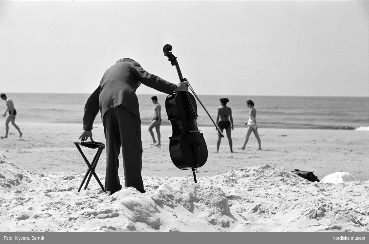 Man iklädd kostym med cello på holländsk sandstrand.