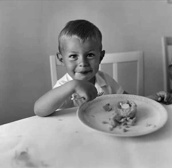 Liten pojke sitter vid matbord med gaffel i handen och matta