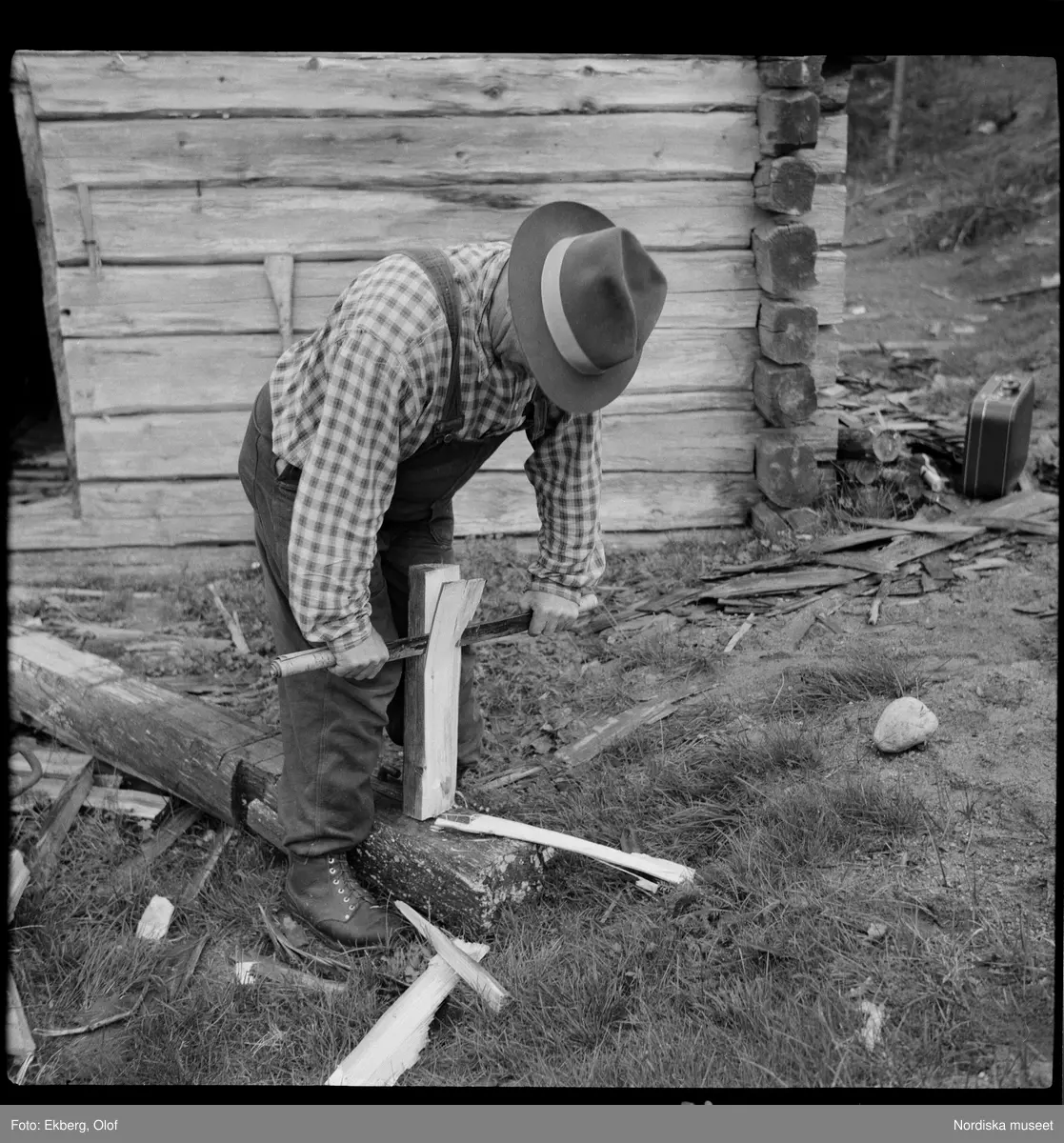 Man utanför knuttimrat hus. Magnus Sundberg, Sjokksjokk, spjälkar takspån.
Norrbottens län. Jokkmokks socken.