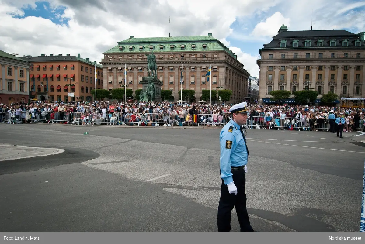 Dokumentation av Kronprinssesbröllopet mellan Kronprinsessan Victoria och Daniel Westling 19 juni 2010. Polis vid Gustav Adolfs torg. I bakgrunden åskådare bakom kravallstaket.