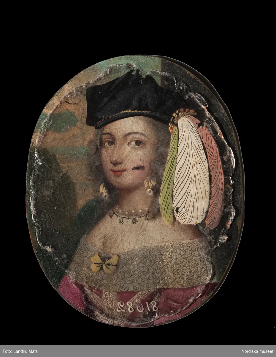 Katalogkort:
"Målning på kopparplåt, osign. Enligt uppgift av givaren föreställande en fröken Hahne. I fodral av svart pressat läder på stomme av papp med 13 glimmerskivor med målade dräkter och dräktdetaljer enligt uppg. målade av prof. N. H. Sjöborg (1767-1838)."
"Blont hår, mörkgrå ögon, rosafärgad klädning besatt med vita spetsar och spetskrage, vitt pärlband i hår och om hals, dessutom juvelhalsband och juvelbrosch. Bakgrund t.h. brunt draperi (vägg?) t.v. träd mot molnig blå himmel, 2 flygande fåglar. Kopparplåten genomborrad upptill. Till detta höra 13 st glimmerskivor att lägga på målningen. I svart ovalt etui, 88 mm x 73 mm av svart refflat skinn, invändigt klätt med ljusblått siden."

Genom att lägga de olika målade glimmerskivorna ovanpå porträttet förändras Kerstin Hahnes utseende. Skivorna visar enligt katalogkort:
- vit turban virad med gulbrunt, ljusbrun draperad dräkt med svarta prickar
- svart huvudbonad och gula örhängen
- svart huvudbonad, ljusröda örhängen, ljusröd bröstrosett
- svart hatt, svart kort jacka, vit krage och vita ärmar synliga i uppslitsningarna
- svart dok och klädning, vit krage
- ljusröd hårprydnad, örhängen vita och ljusröda, svart klädning med vit krage
- ljusbrunt hårnät, dito örhängen med vita pärlor, ljusbrun klädning med vita ärmar
- vitt nunnedok, svart dräkt
- ljusbrun hårprydnad, möjligen nät av band, vita örhängen, svart klädning, vit krage
- brun huva med krage, möjligen kappa
- svart barett med en grön, en vit och en rosafärgad plym, fästade med en gul agraff, vita örhängen, vit bröstrosett
- hårklädsel av 3 gula fjädrar samt en gul, en vit, och en grön plym, svart mask, vita örhängen, vitt band som täcker hakan, två gula bröstrosetter
- hårprydnad (nät?) ljusrött, röd och vita örhängen, till venster en neger, som omfamnar damen, under negerns huvud något gulvitt, som möjligen tillhör hans dräkt

Kerstin Hahne, död 1656, gift med Honorat Verdelet, var dotter till uppvaktaren hos kung Karl IX:s barn, Christoffer Hahne till Hesselby och Ingrid Björnsdotter.