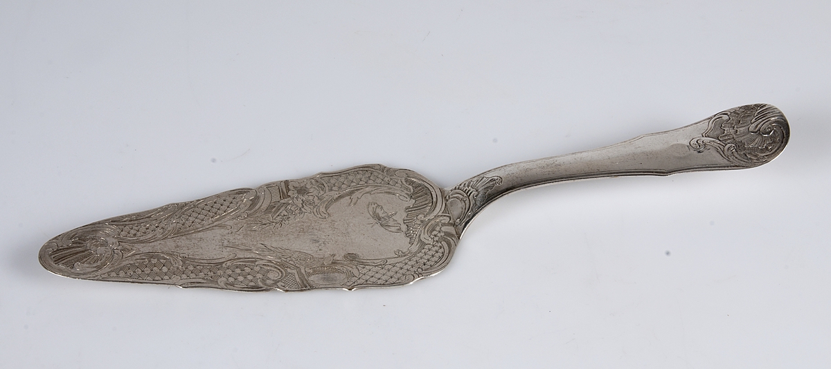Tårtspade av silver. Graverat: MD (MD står för Matthias Dubois). Stämplar: B, tre kronor, St Erik, LAMPA. Stämplad: JC.