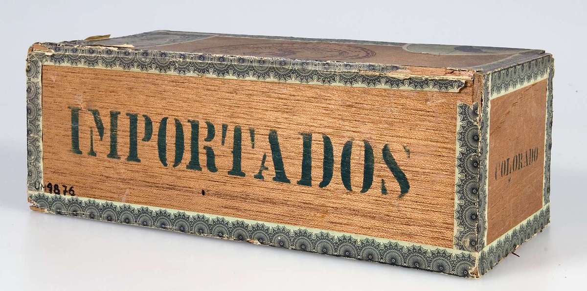 Papperslister i grönt och svart. Text på lockets pappersetiketter: Flor de Cuba. På locket en stämpel med texten: Havanna Magasinet Stockholm; Flor de Cuba, samt en örn. Blyertsanteckningar på locket: Till julgran. På framsidan i grönt tryck: 100, No 1. Fodrad med grönt papper. På lockets insida ett byggnadsmotiv i svart, på skyddsbladet en örn i svart.