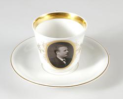 Kopp. Vitglaserad med dekor i guld och svart tryck. Fotografi av handelsbokhållare Hugo Wijkman, som till omkring 1908 var anställd hos cigarrhandlare Carl Peschel-Barowiak.

