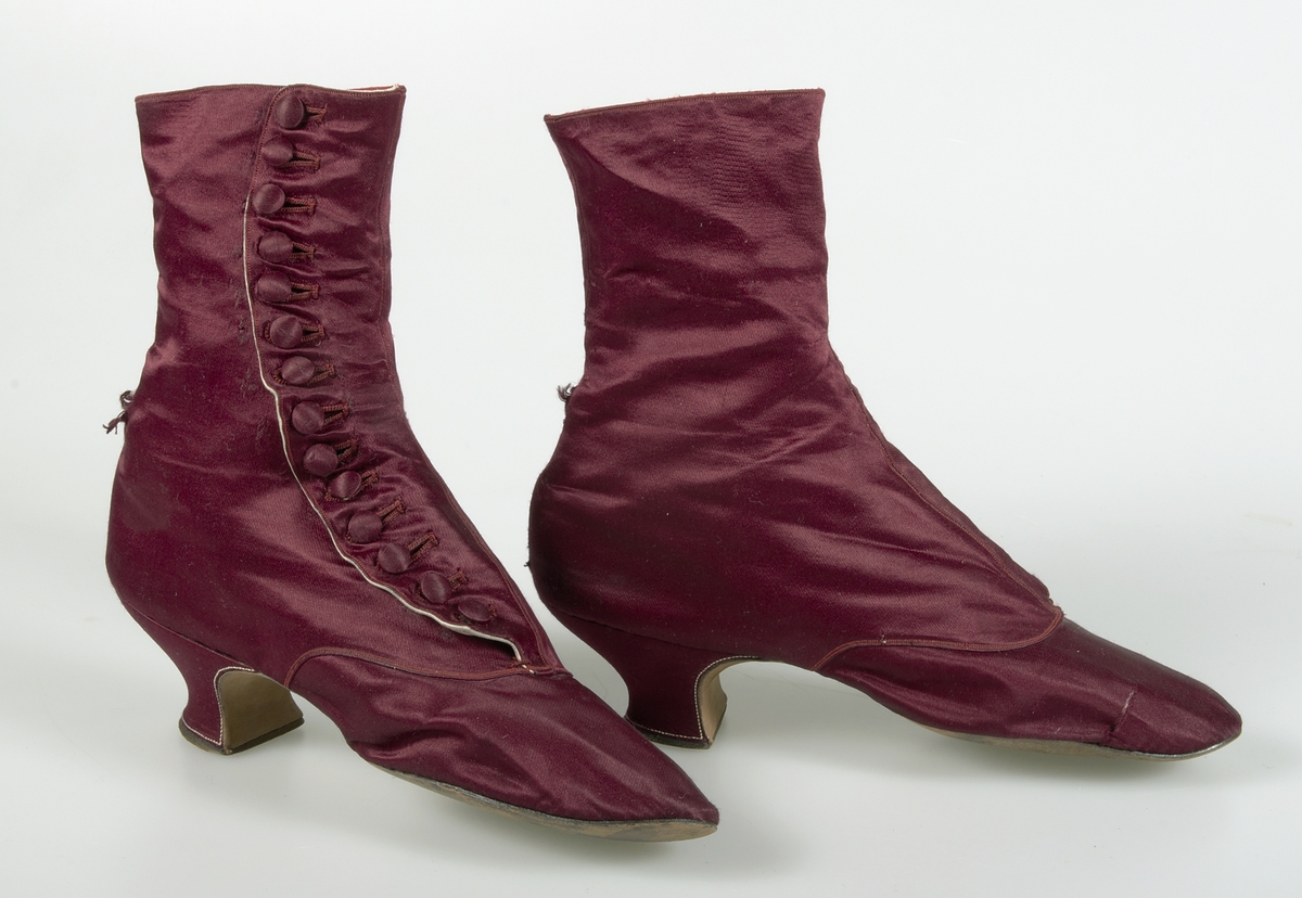 Kängor av vinrött siden. Knäppt med 14 klädda knappar. Brun lädersula. Fodrade med vit lärft, vitt skinn och rött siden.