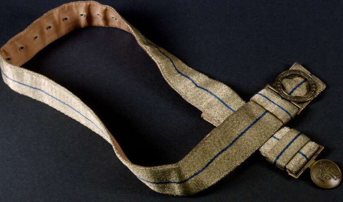 Uniform av diagonalvävt ylletyg. Guldgaloner och gradbeteckningar av gulmetall. Knappar av gulmetall med riksäpple. Fodrad med grått konstsiden. Skärp av brunt läder med axelrem. Skärp av metalltråd i guld och blått, läderfodrat, mässingsspänne. Uniformsmössa av grått kypertvävt ylle. Svart läderskärm, guldsnodd. Mässingsknapp och emaljkokard. Text: Arméns centrala beklädnadsverkstad. Skärmmössa med skärm av tyget. Båtmössa.