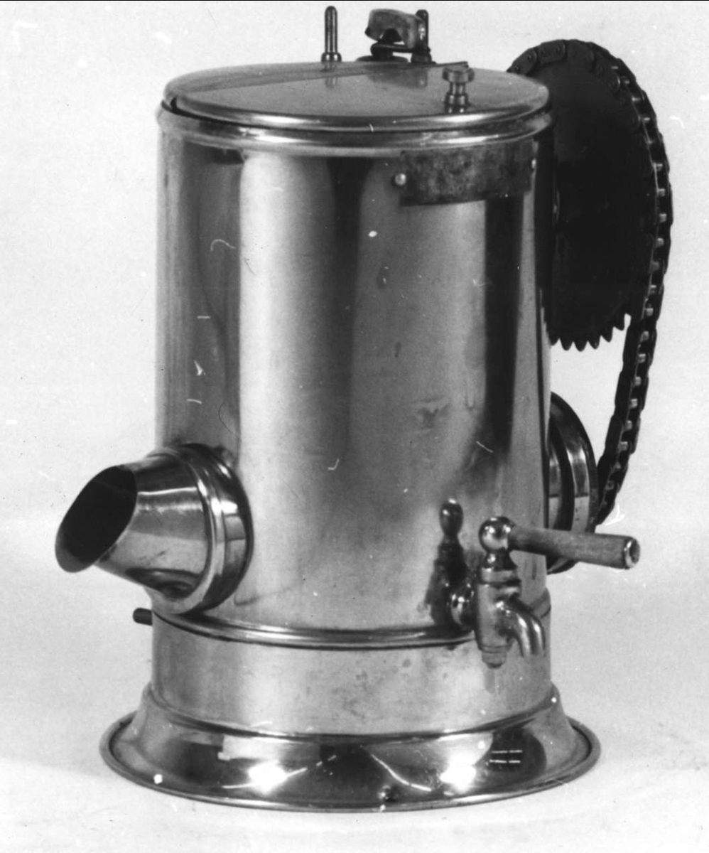 Tvålskumsapparat av rostfritt stål (behållaren), och förnicklad mässing. Handtag av trä. Mässingsplakett med text: Tvålskumsapparaten AROS, patenterad, A. LÖÖF, Västerås. Till apparaten hör en lös brunglaserad porslinskontakt. Uppvärmes med elektricitet. 
