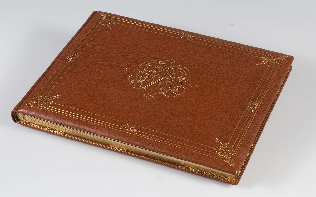 Album, inbundet i helfranskt band i brunt läder med stämplade ramverk och ornament i guld. På pärmens framsida spegelmonogram, komponerat av bokstäverna GEK (Gustaf E. Karlsson). Guldsnitt runt om, blad av mörkgrå kartong. Frontespis med textad tillägnan: "Till Direktör Gustaf  E. Karlsson 60-årsdagen 19 30/10 28. Med varm lyckönskan och tack för värdefullt arbete. Uppsala Specerihandlarförening". Albumet innehåller fotografier av Gustaf E. Karlsson, av hans speceriaffär, av styrelsen i Uppsala Specerihandlarförening samt av föreningens hedersledamöter och medlemmar. Albumet på pärmens baksida stämplat: "Levins Bokbinderi. Uppsala Bokband C W Bergman". Mapp, klädd med mörkbrunt läder. 