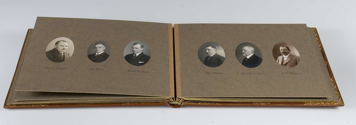 Album, inbundet i helfranskt band i brunt läder med stämplade ramverk och ornament i guld. På pärmens framsida spegelmonogram, komponerat av bokstäverna GEK (Gustaf E. Karlsson). Guldsnitt runt om, blad av mörkgrå kartong. Frontespis med textad tillägnan: "Till Direktör Gustaf  E. Karlsson 60-årsdagen 19 30/10 28. Med varm lyckönskan och tack för värdefullt arbete. Uppsala Specerihandlarförening". Albumet innehåller fotografier av Gustaf E. Karlsson, av hans speceriaffär, av styrelsen i Uppsala Specerihandlarförening samt av föreningens hedersledamöter och medlemmar. Albumet på pärmens baksida stämplat: "Levins Bokbinderi. Uppsala Bokband C W Bergman". Mapp, klädd med mörkbrunt läder. 