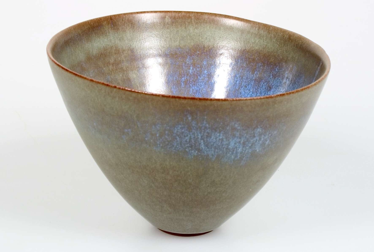 Skål utförd av Ingrid Atterberg omkring 1950. Av sintergods med ljus, krakelerad glasyr i beigeljusblått. Mynningen ej parallell med bottnen.